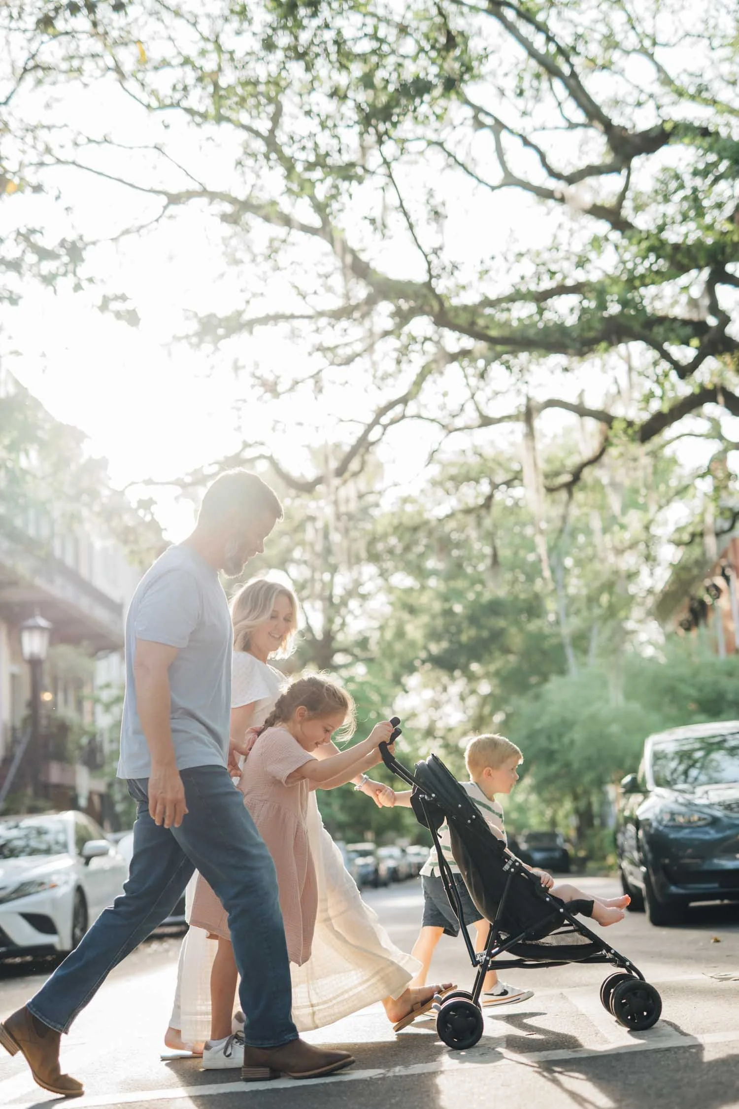 Two parents walking with their daughter while pushing a stroller along a neighborhood sidewalk during a lifestyle family photography session in Raleigh–Durham.