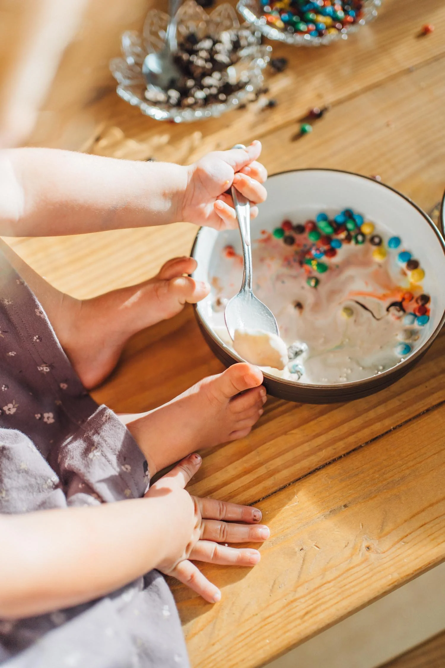 Close-up of a toddler’s hand holding a spoon in a bowl of cereal during an everyday family photography moment at home.