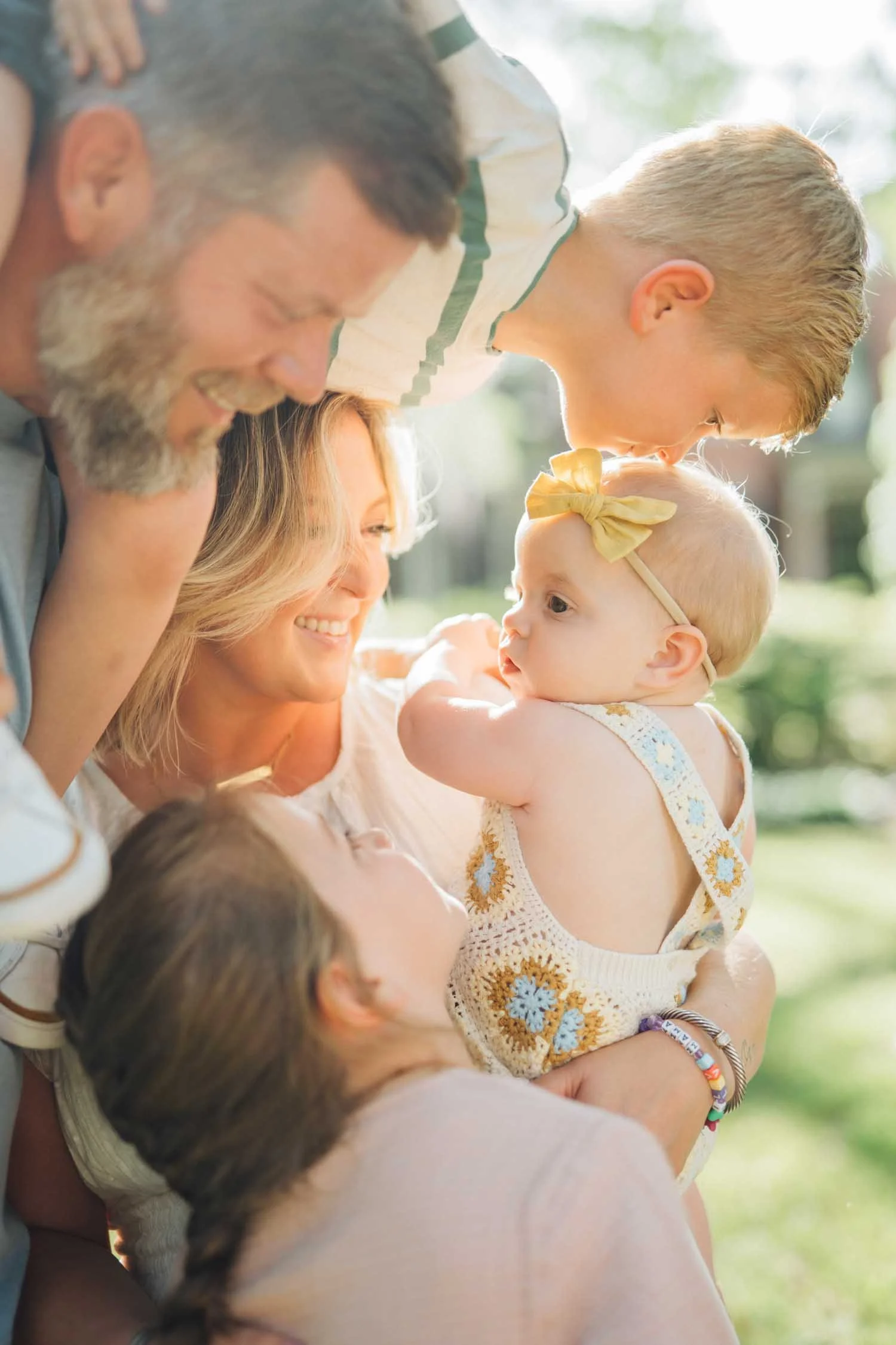 Parents holding their three children and kissing their baby outside during a joyful family photography session in Raleigh, NC.
