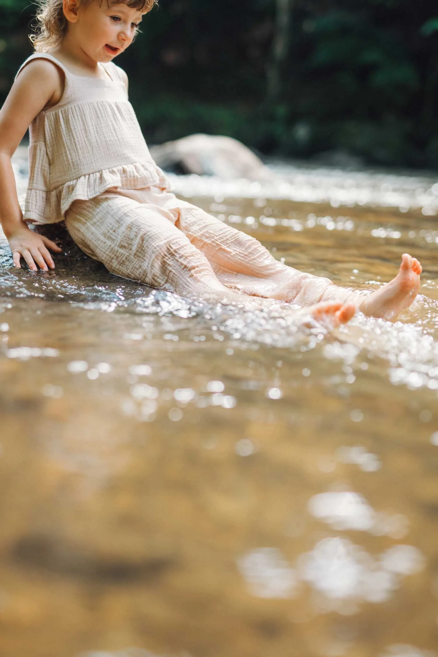 Toddler kicking her feet in a shallow creek during a relaxed lifestyle family photography session in Raleigh–Durham.