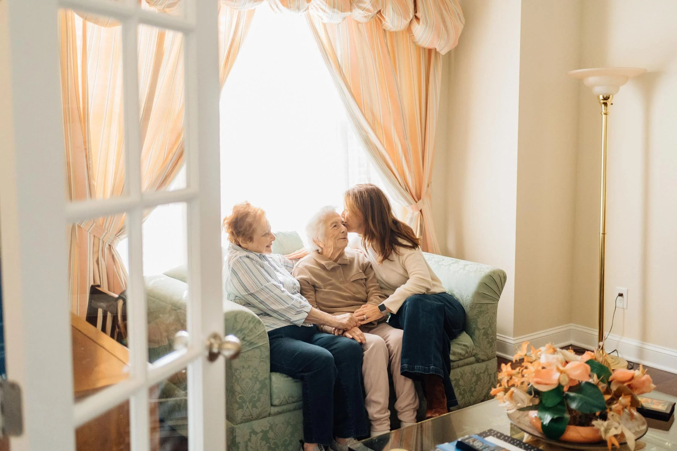 Three women from different generations sitting together on a couch holding hands during a multi-generational family photography session.