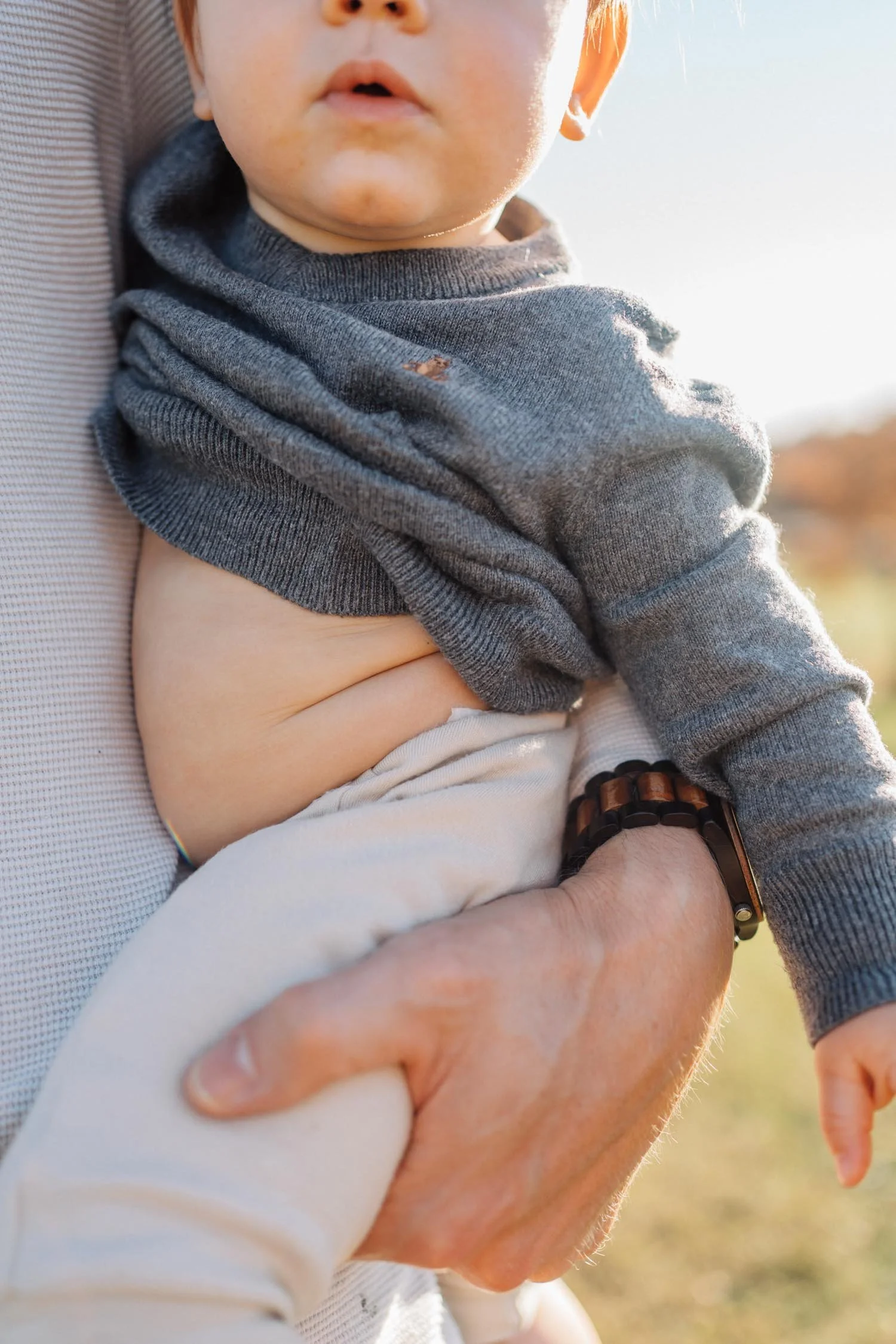 Close-up of a parent holding a baby outdoors at the park during a natural family photography session in Raleigh, North Carolina.