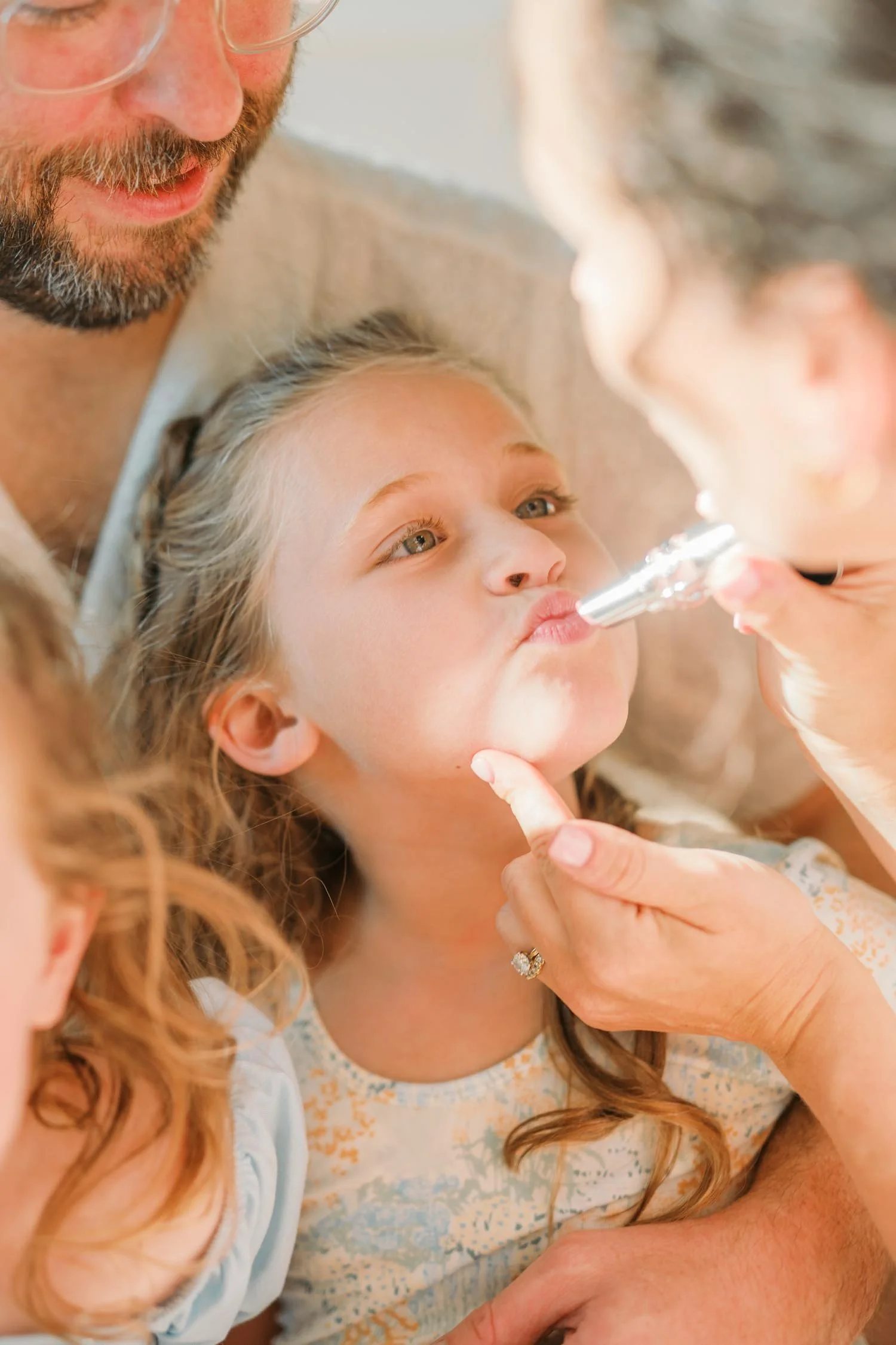 Mother helping her daughter put on makeup inside their home during a relaxed backyard family photography session in the Raleigh–Durham area.