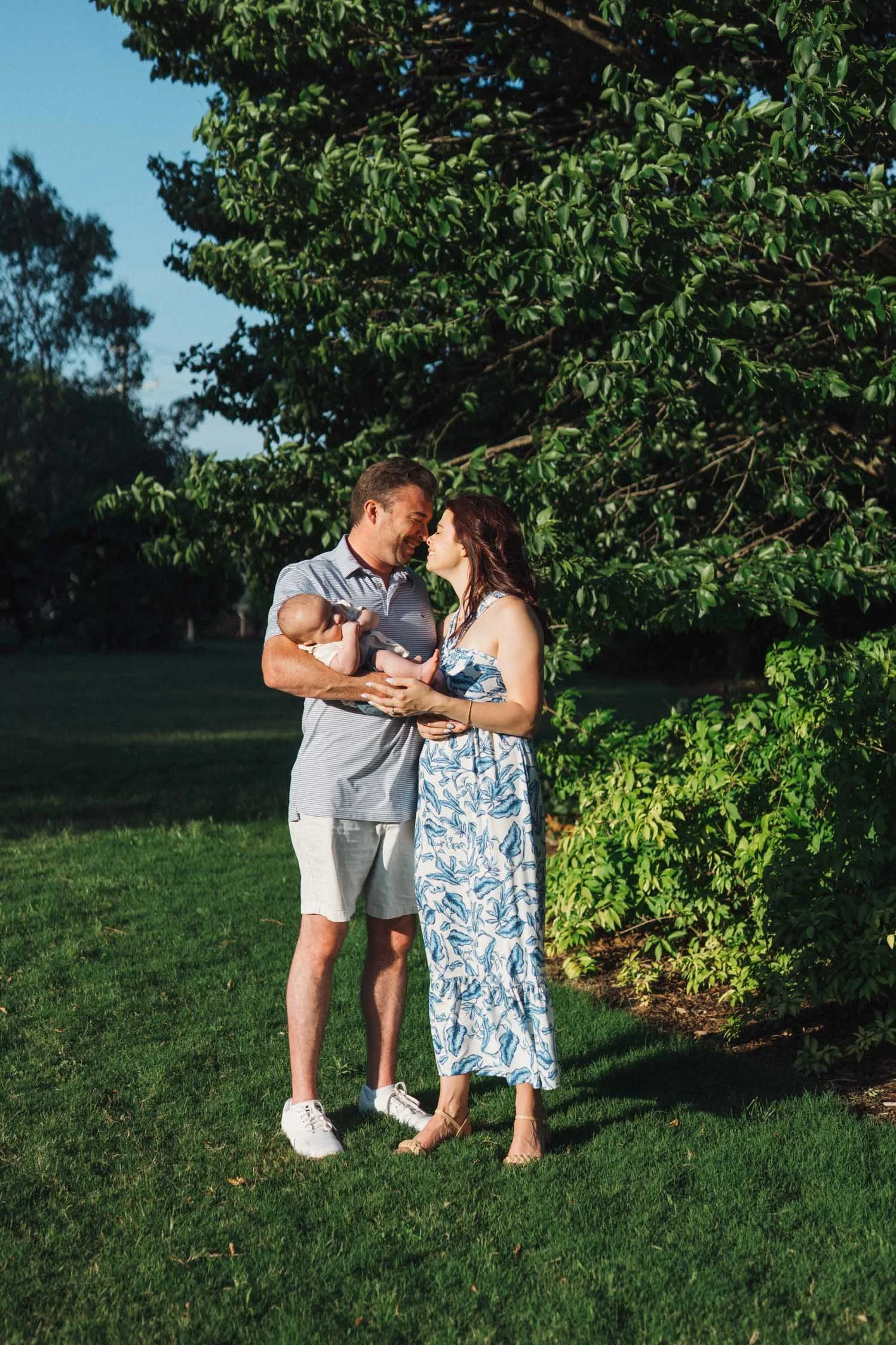Two parents holding their baby together in their yard during a relaxed family photography session in Raleigh, North Carolina.
