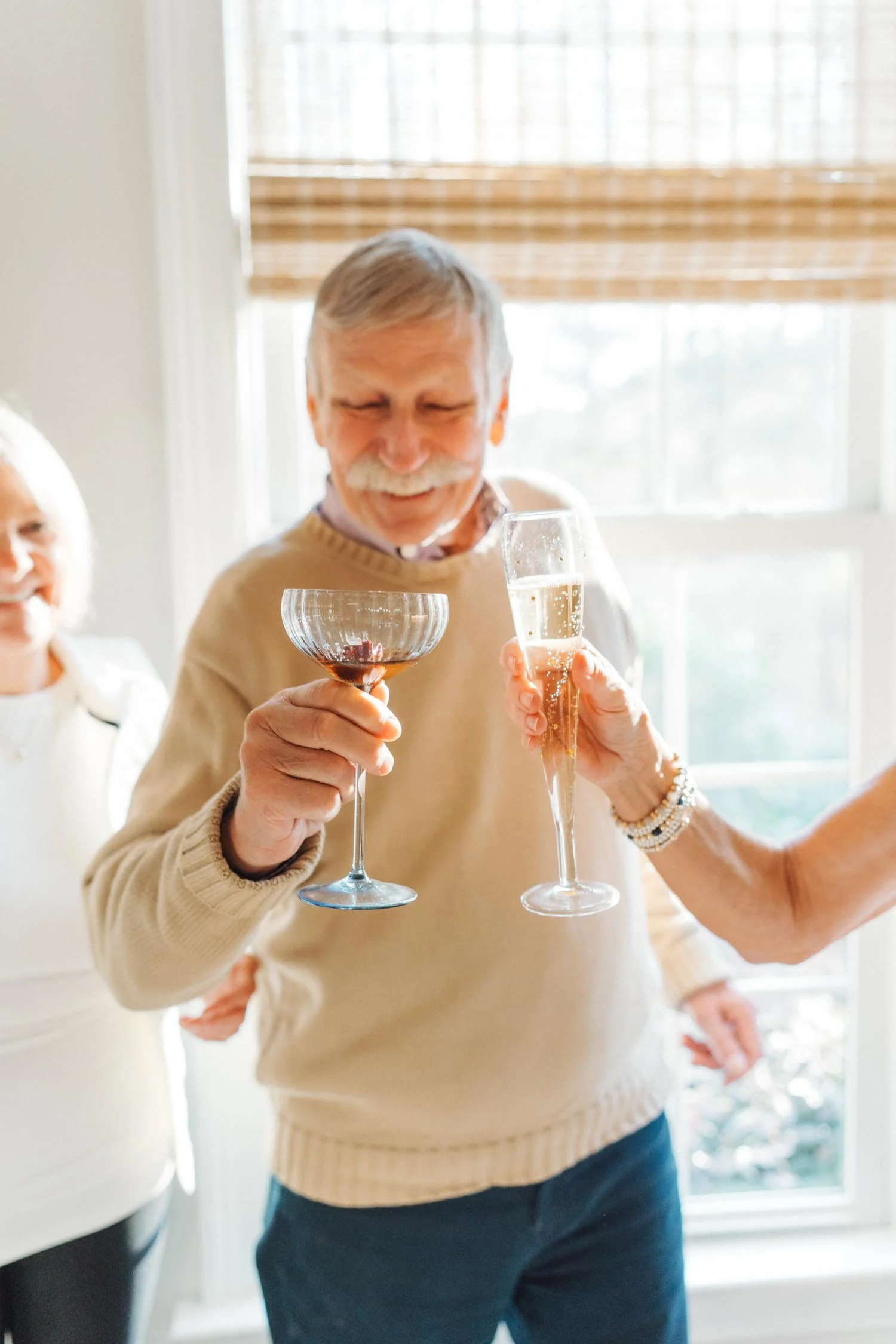 Grandparents and parents clinking cocktails together in the kitchen during a multi-generational family photography session at home in Raleigh, NC.
