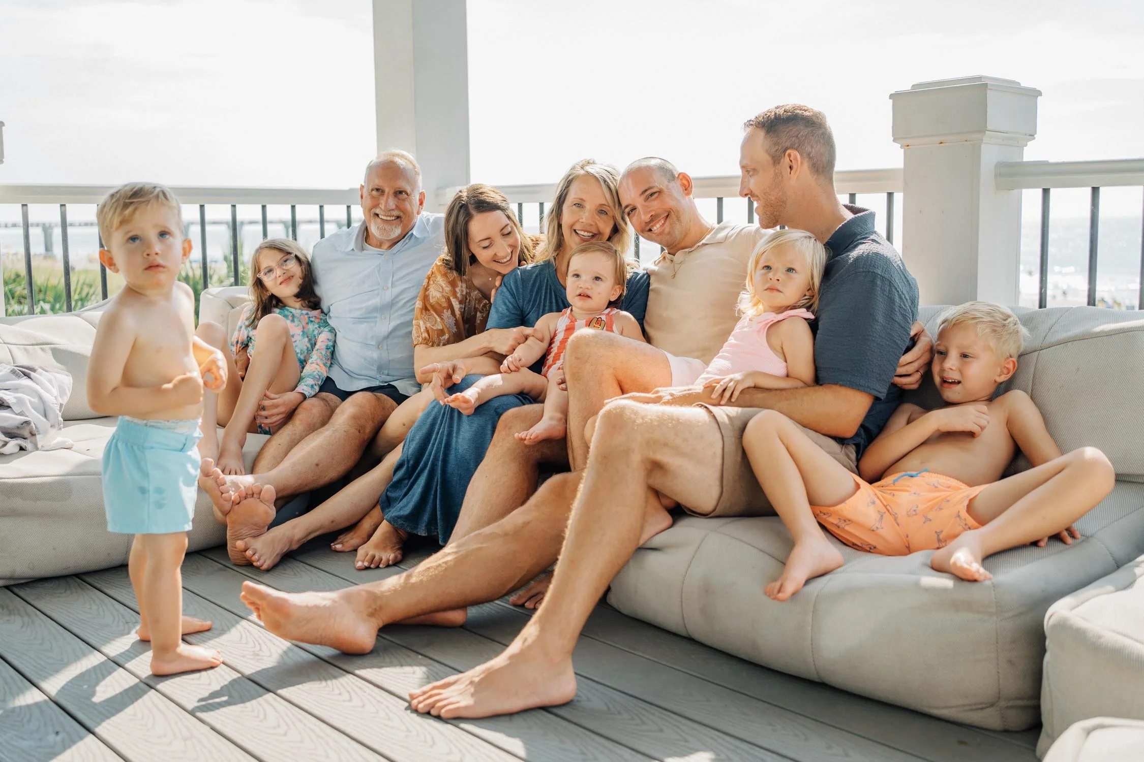 Three generations of a family lounging together on porch couches during a relaxed multi-generational family photography session in Raleigh, NC.