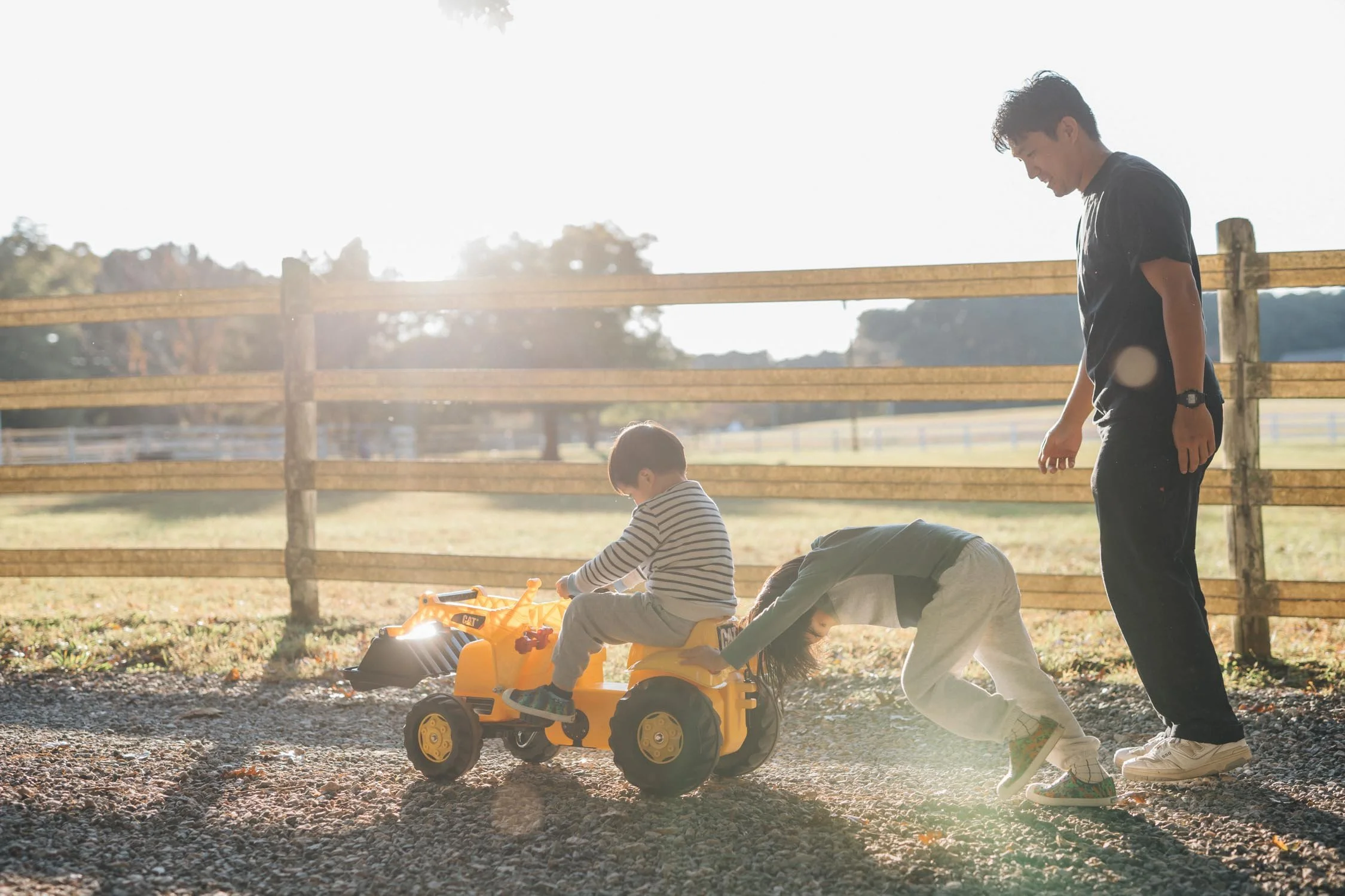 Two children pushing a toy tractor together in their backyard during a playful family photography session in Raleigh, NC.