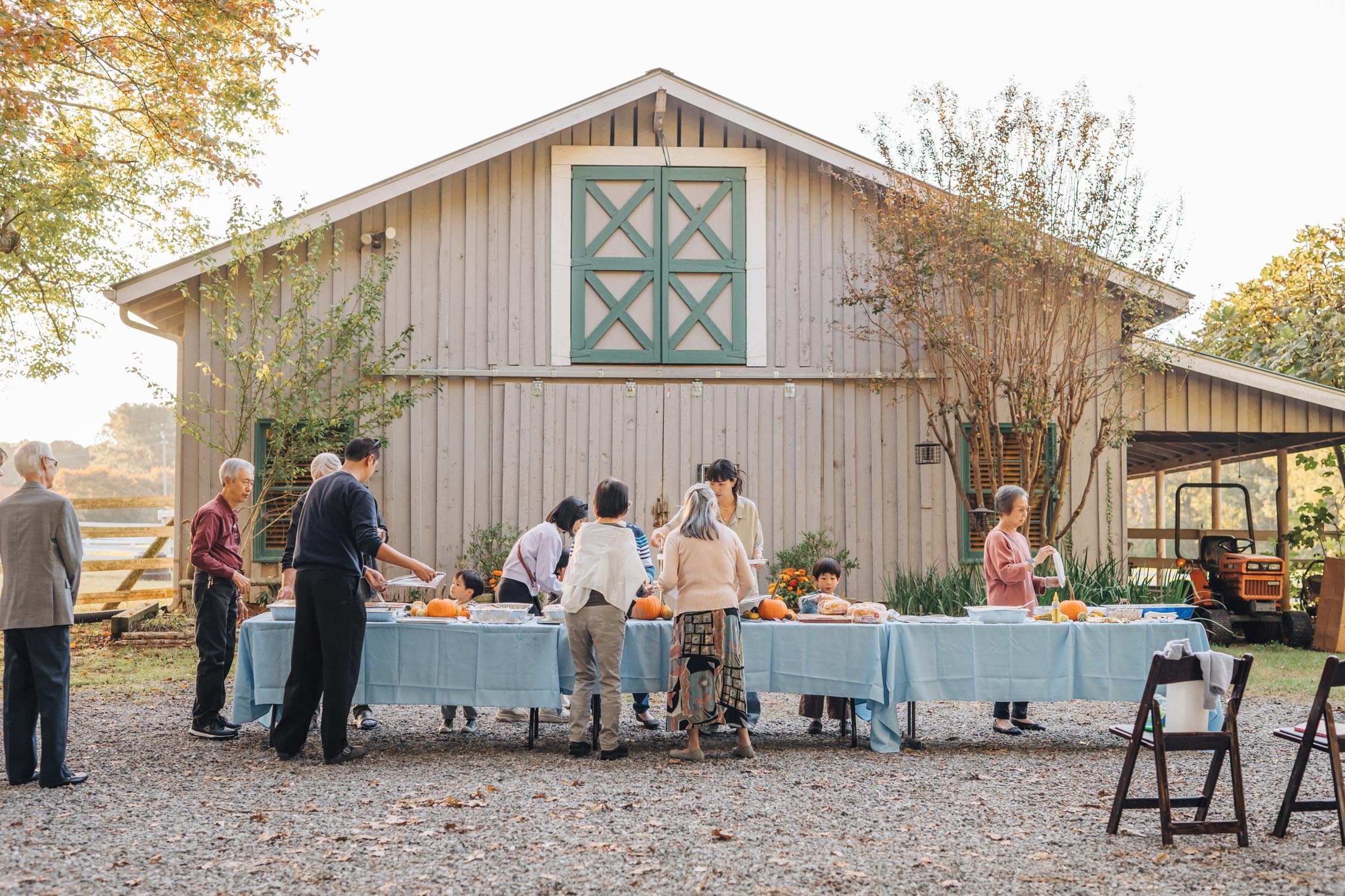 Long dinner table surrounded by family outdoors near a barn during a multi-generational family photography session.