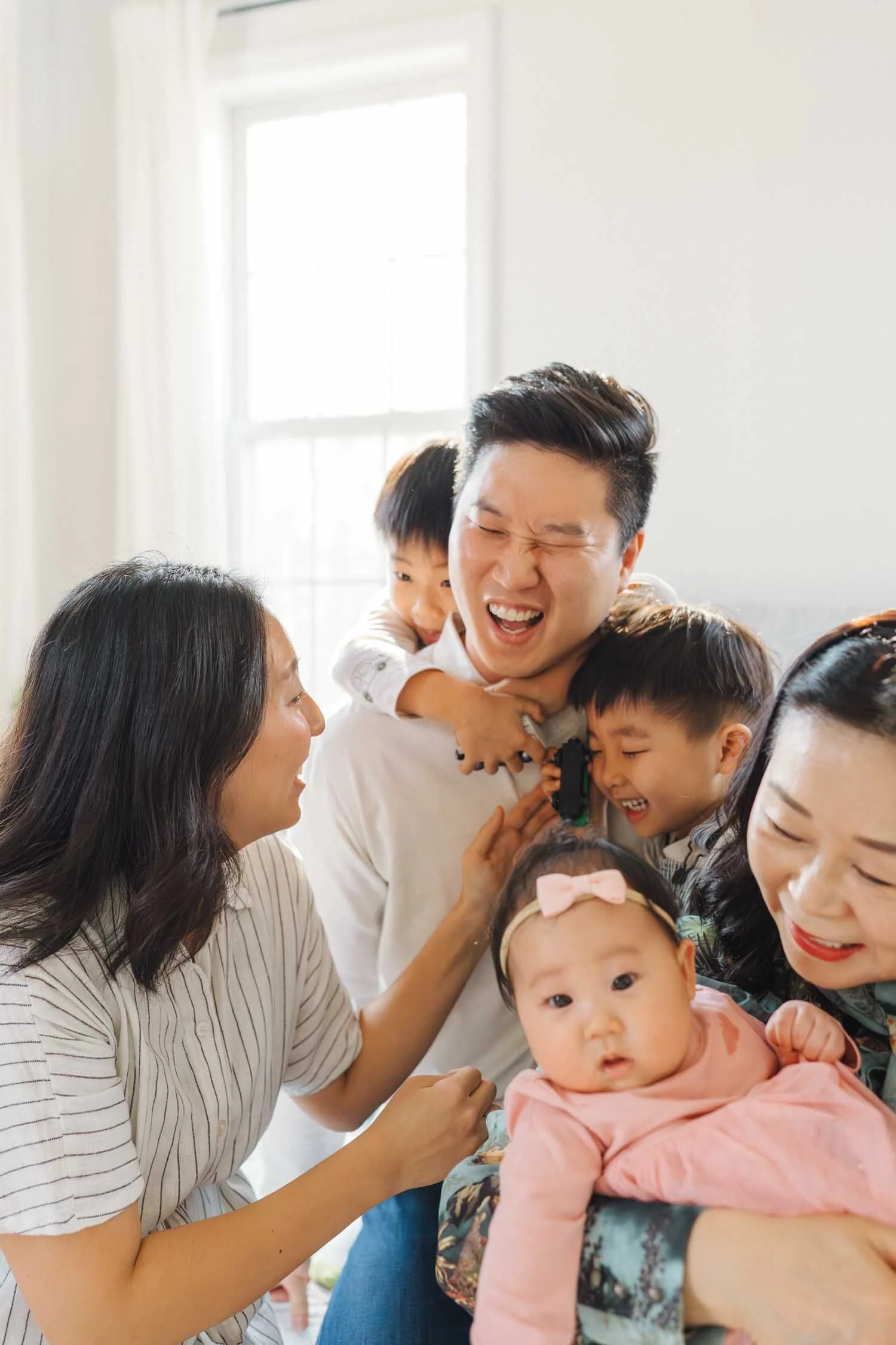 Parents laughing while juggling their three children inside their home during a joyful family photography session by Autumn Brooke Photography.