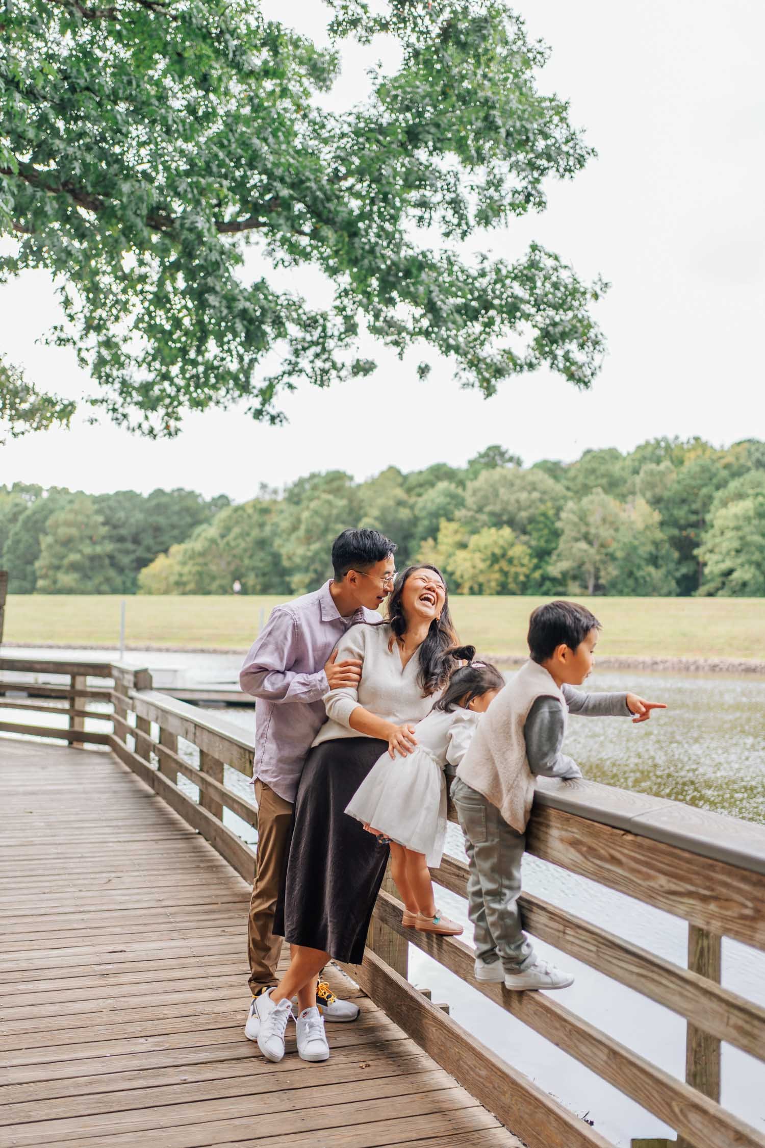 Family standing together on a pier as parents laugh and children look out at the water during a lifestyle family photography session in Raleigh–Durham.