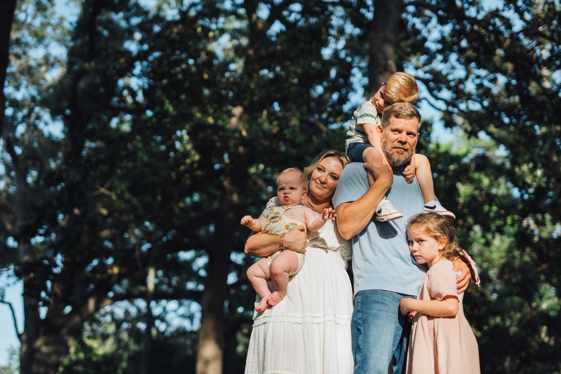 Parents standing in a park with their children sitting on their shoulders during a relaxed family photography session in North Carolina.