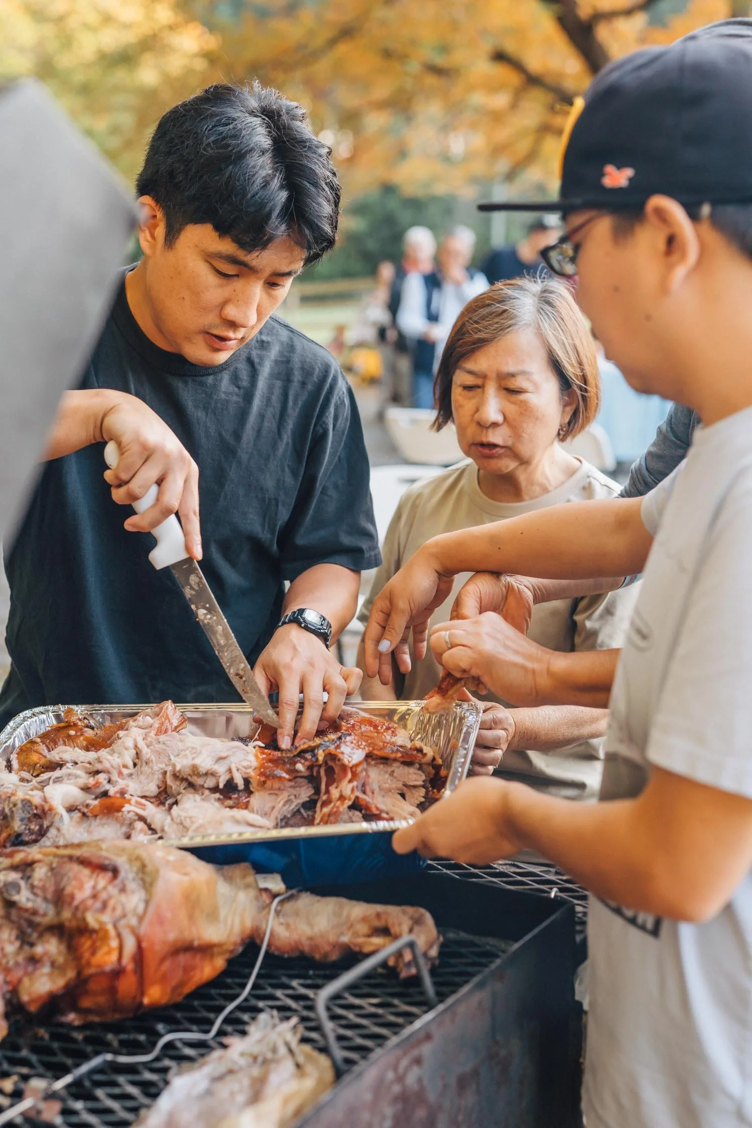 Grandparents and parents carving food together beside a backyard grill during a multi-generational family photography session in Raleigh, North Carolina.