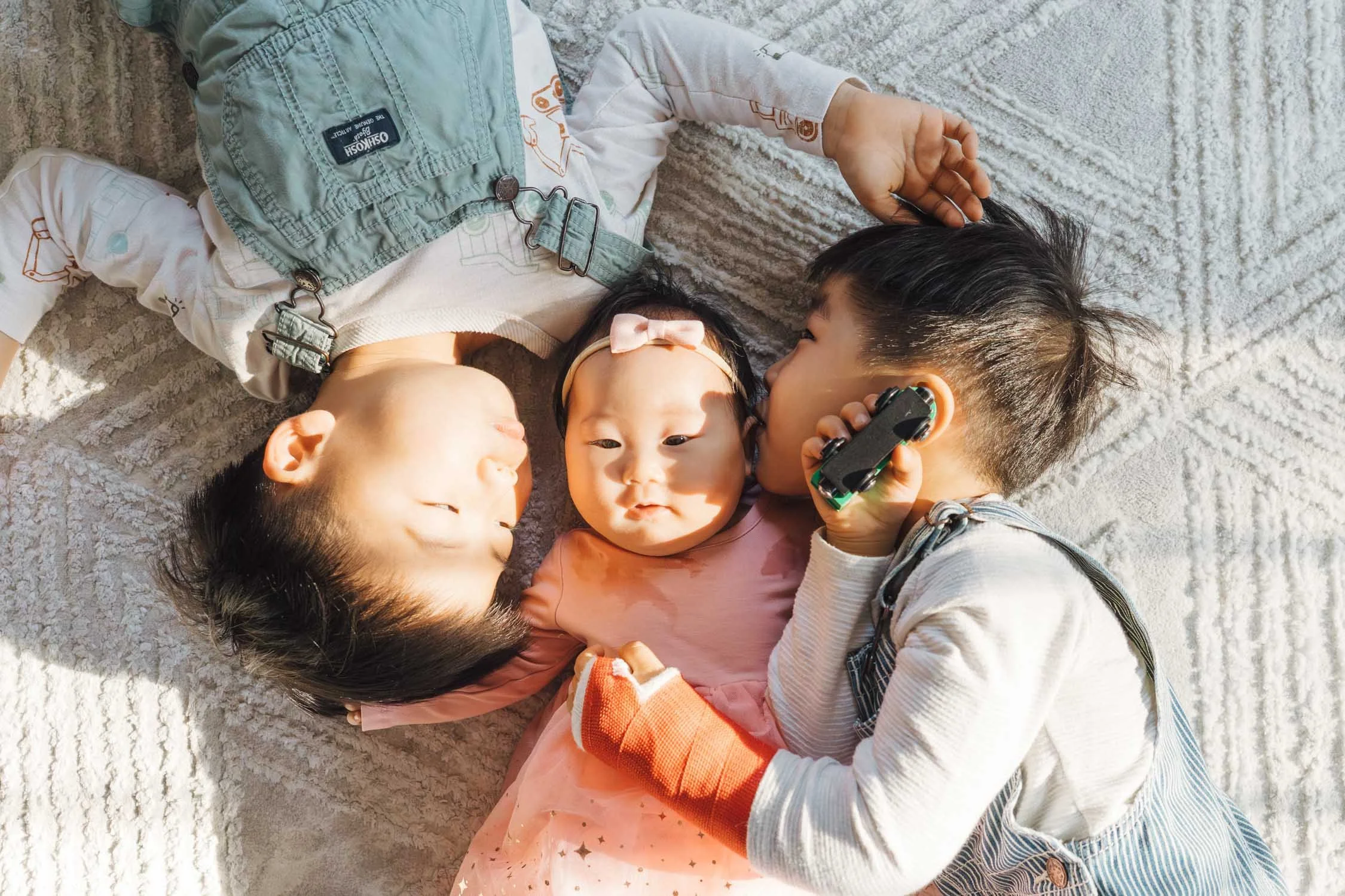 Three children lying on the floor playing with toys inside their home during a signature Backyard family photography session in Raleigh, North Carolina.