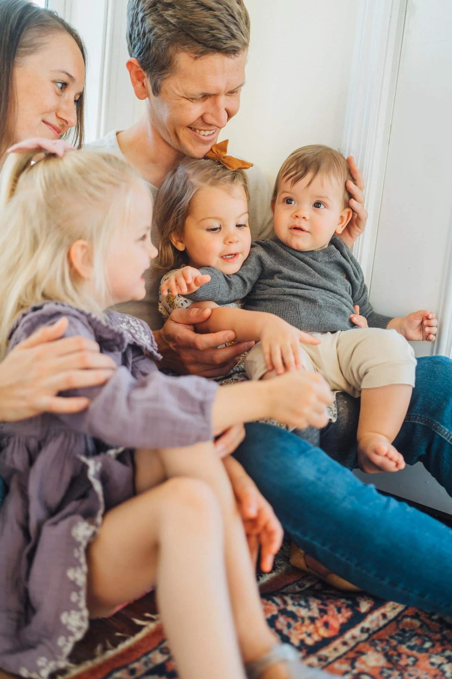 Parents sitting at home with their three children on their laps during a relaxed in-home family photography session in Raleigh–Durham.