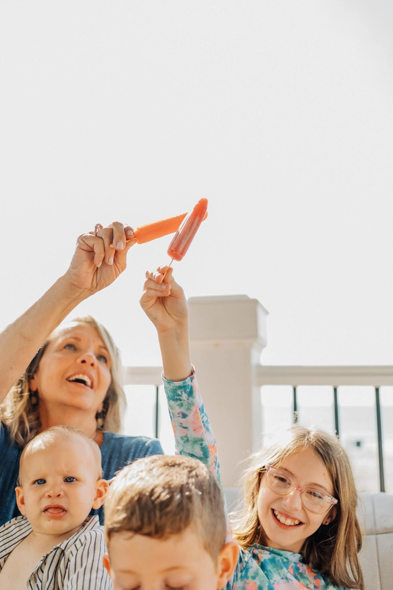 Mother enjoying popsicles with her children on the deck during a natural family photography session in Raleigh–Durham.