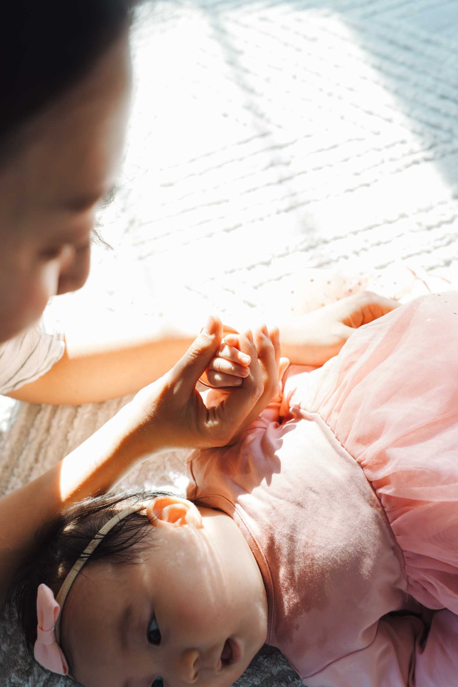 Close-up of a baby girl resting on her mother’s lap on the floor at home during a family photography session in Raleigh–Durham.