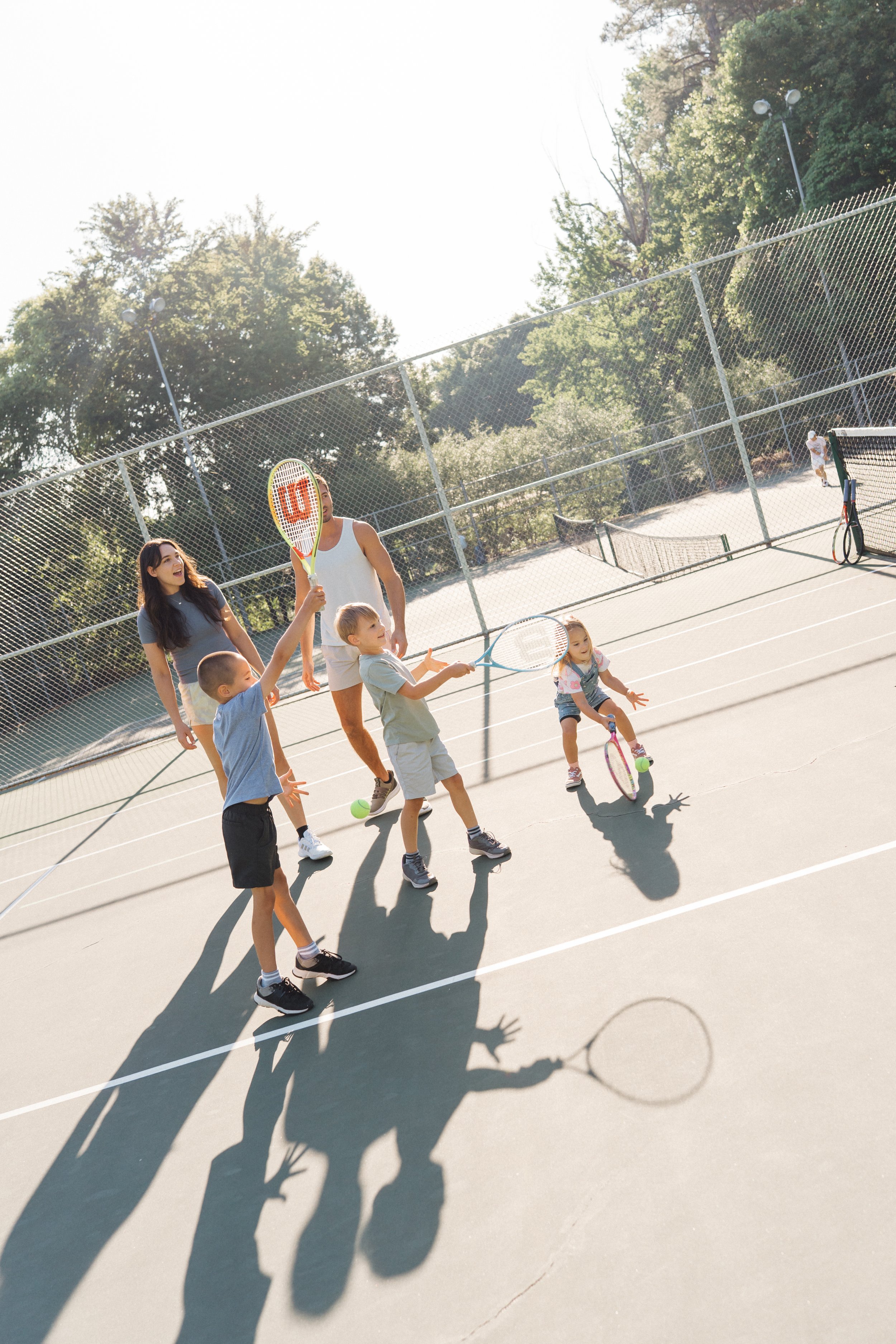 family with 3 kids playing tennis at a tennis court in Raleigh,NC for storytelling family photos