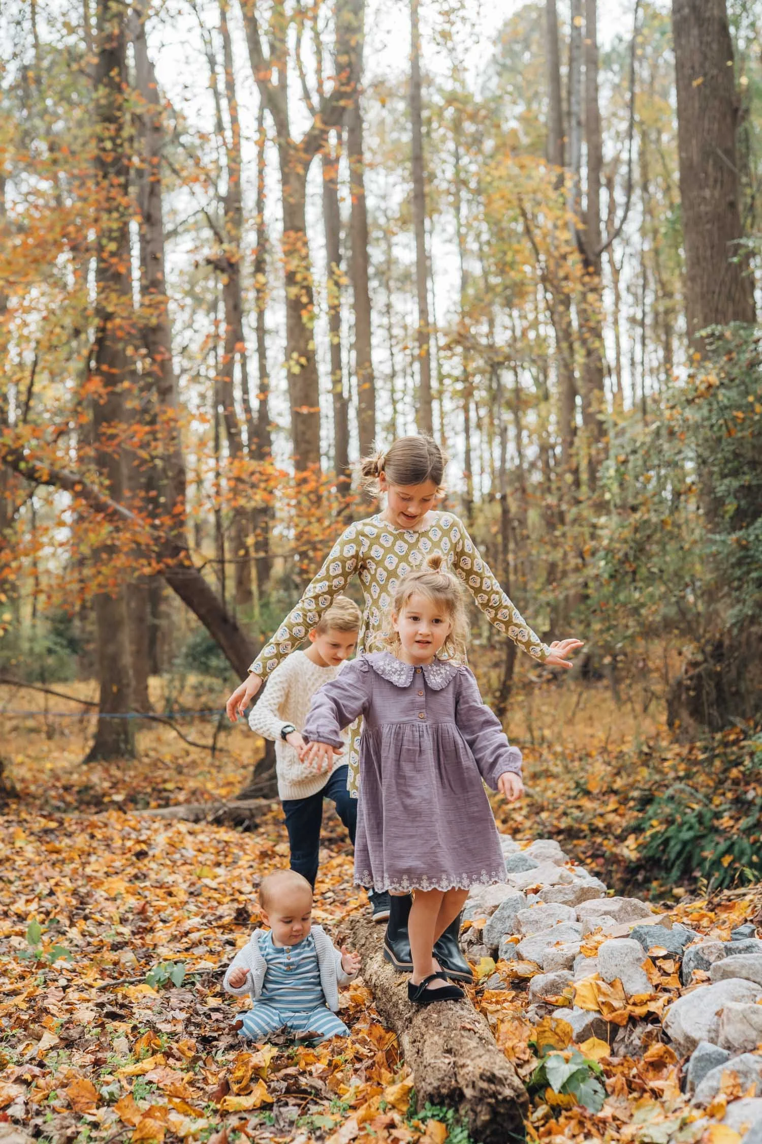Four children walking together through fallen leaves in the woods during a natural family photography session in North Carolina.