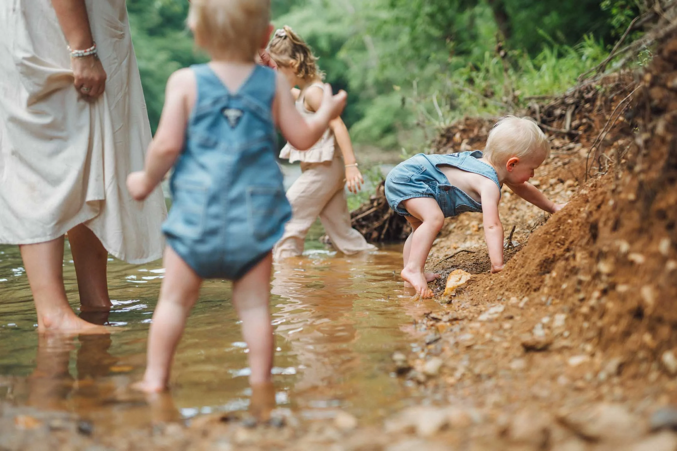 Three young children playing together among rocks on a riverbank during a natural family photography session in North Carolina.