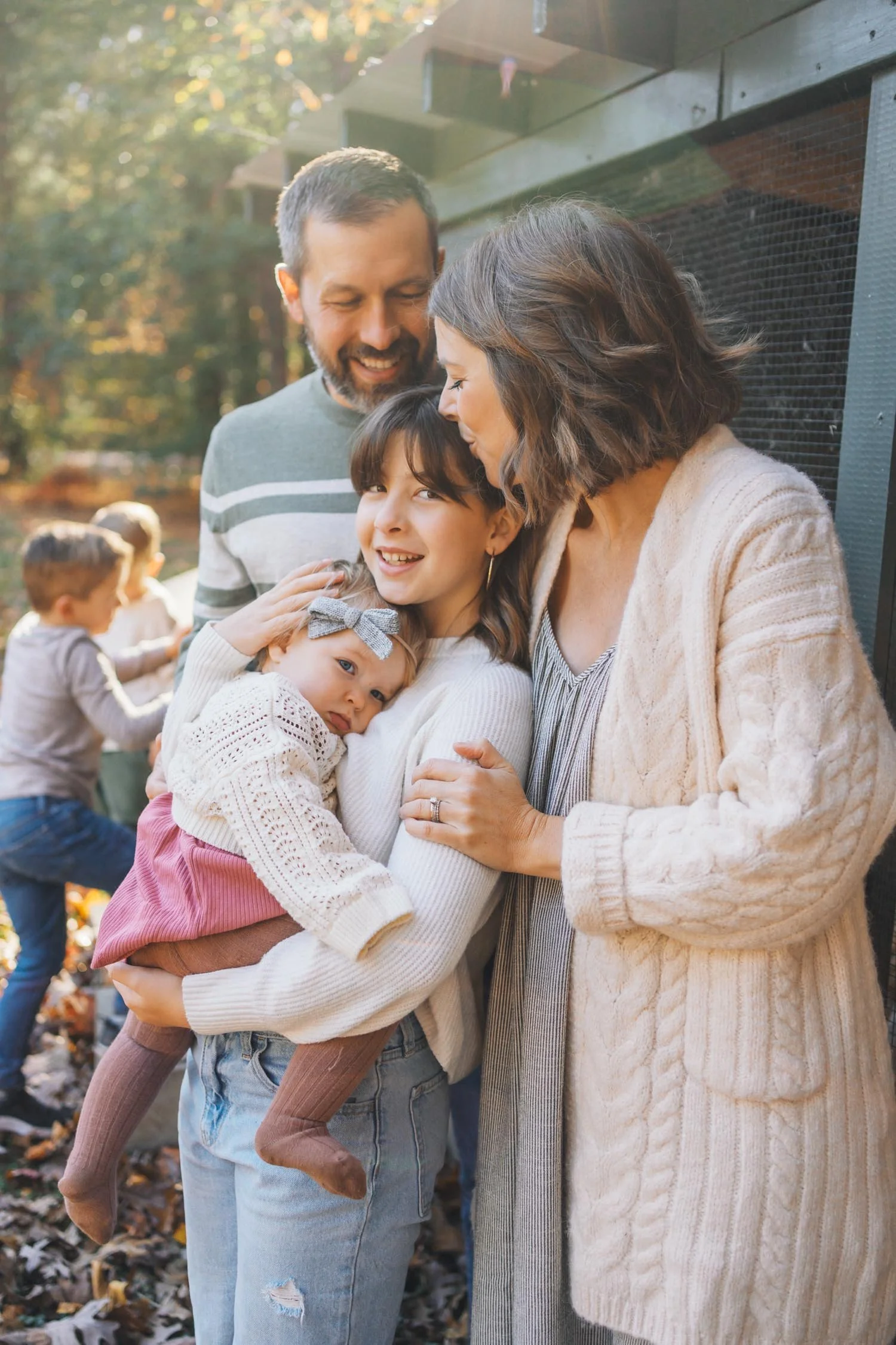 Two parents smiling at their pre-teen child while the child holds a baby during a candid family photography session in North Carolina.