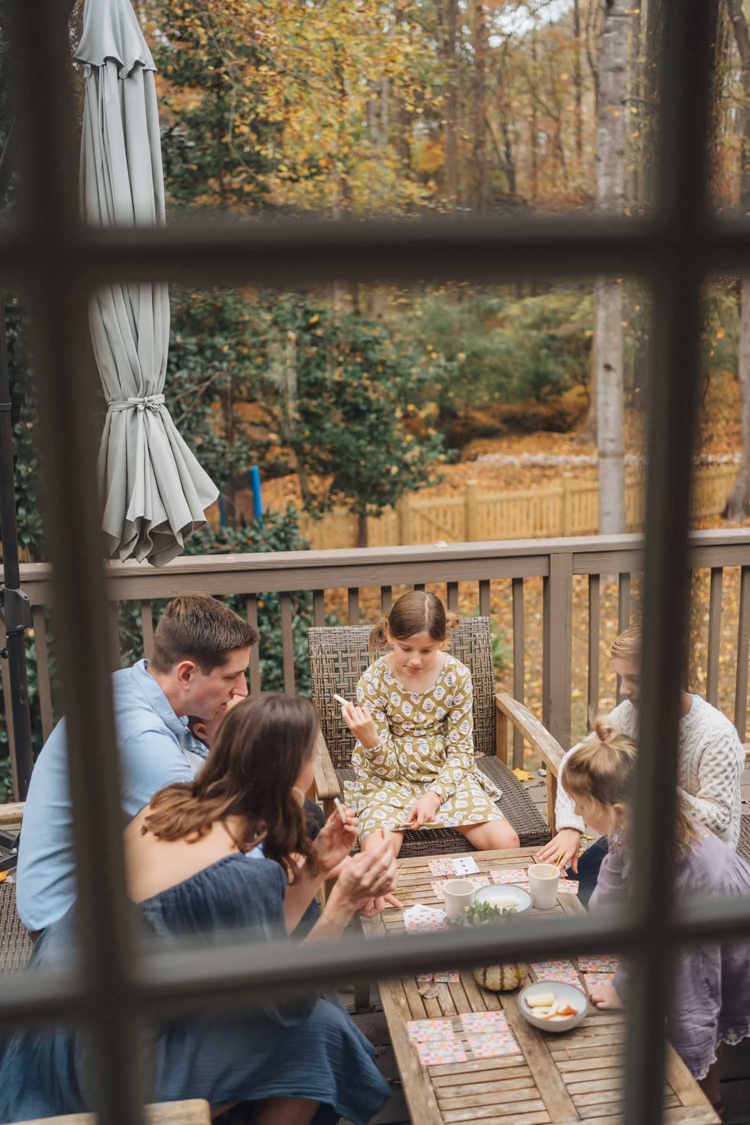 View through a window of a family playing a game together outside during a lifestyle family photography session in Raleigh–Durham.