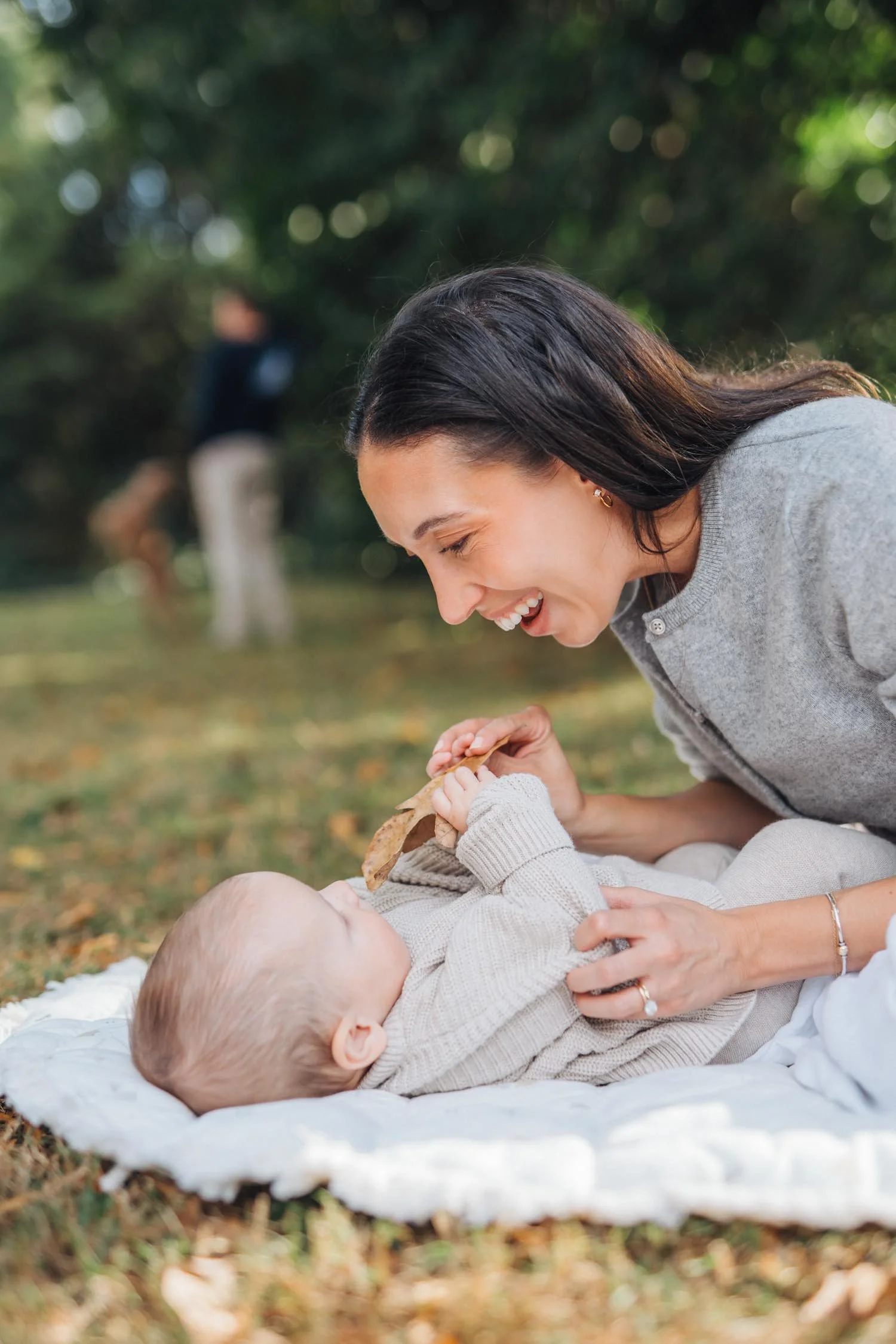 Mother smiling down at her baby lying on a blanket in the grass during a backyard family photography session in Raleigh, North Carolina.
