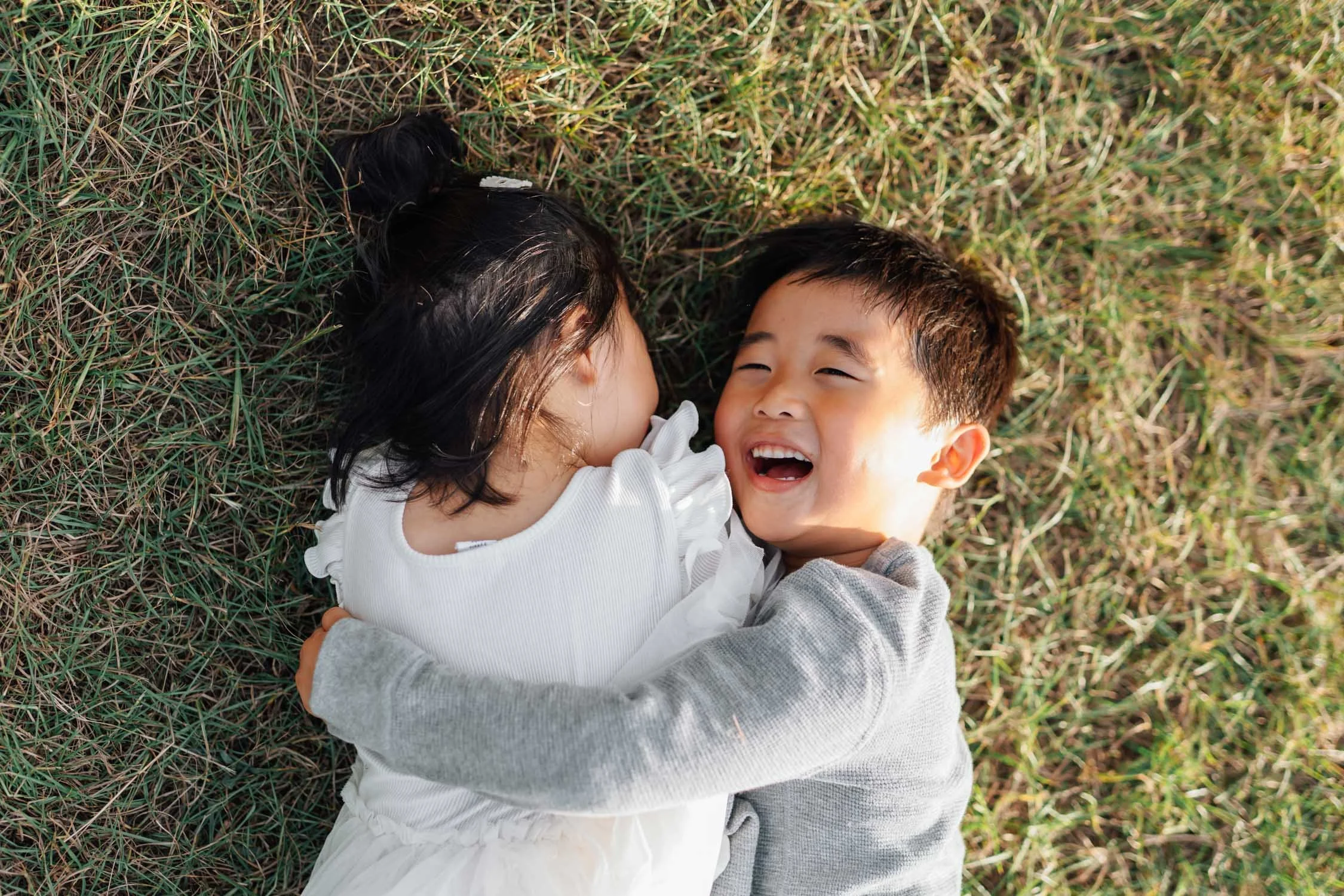 Two children lying on the grass together and playing during a relaxed family photography session in North Carolina.