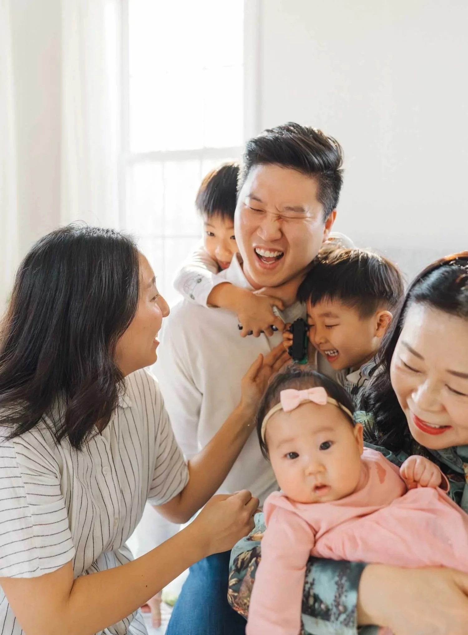 Two parents laughing while wrangling three children inside their home during a candid family photography session by Autumn Brooke Photography.