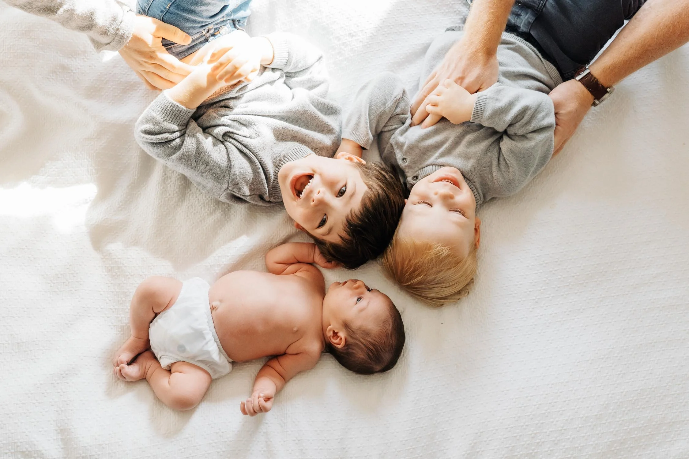 Three children laughing together while lying on a bed at home during a candid family photography session by Autumn Brooke Photography in Raleigh, NC.