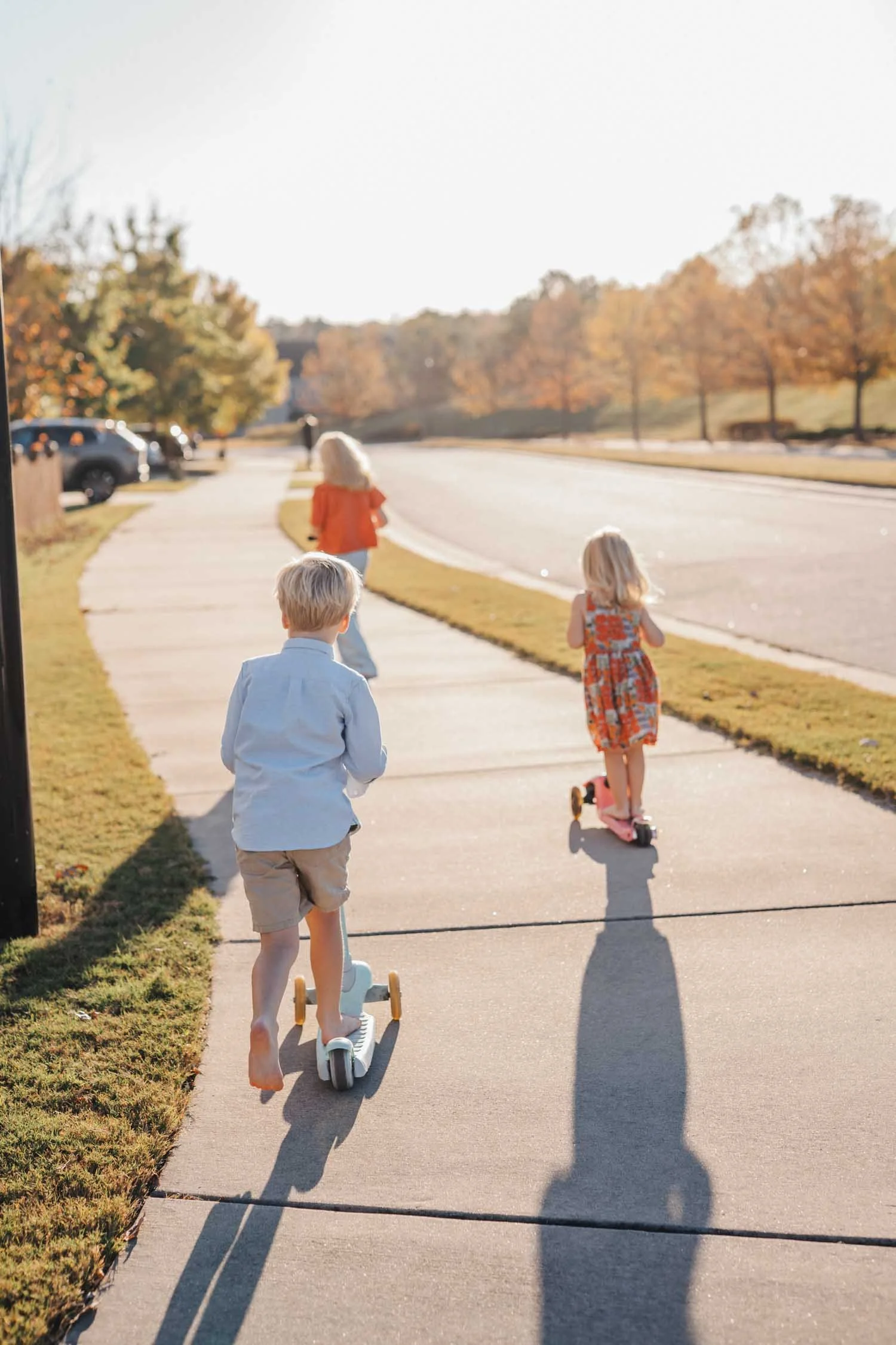Three children riding scooters along a sidewalk during a candid family photography session in the Raleigh–Durham area.