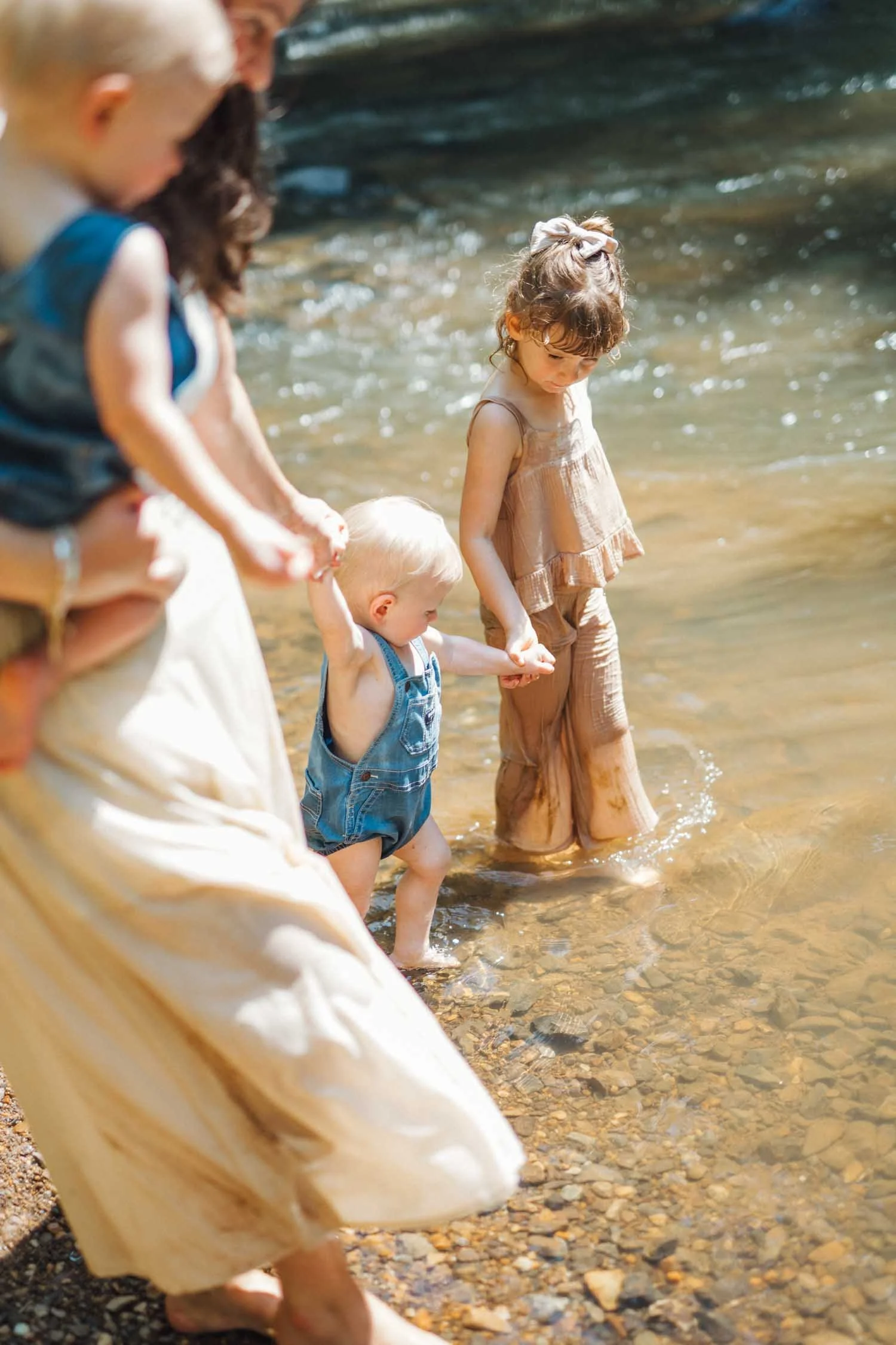 Mother and three young children walking together through a shallow creek during a Locals family photography session in Raleigh–Durham.