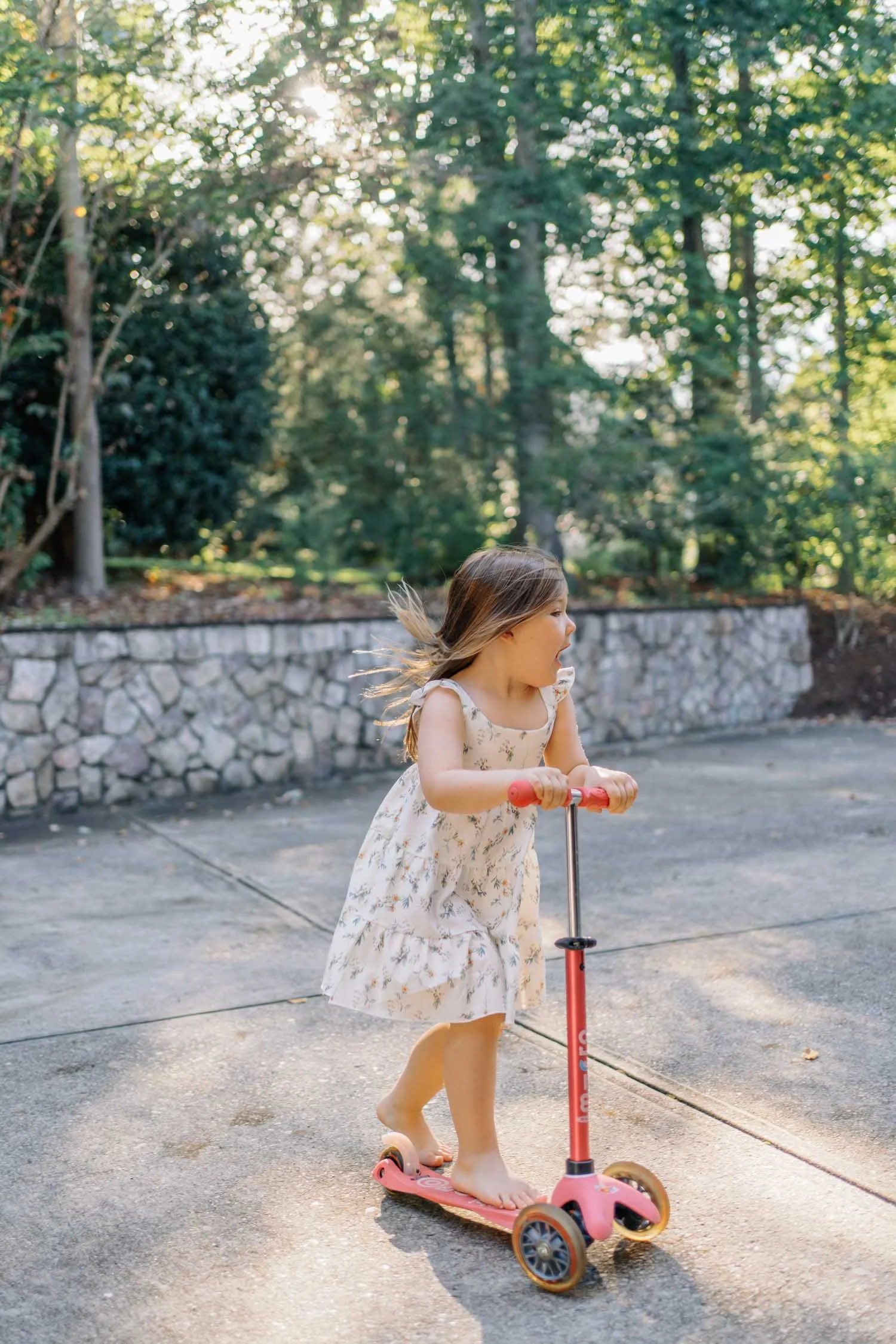 Little girl riding her scooter in the driveway during a playful family photography session in Raleigh–Durham.