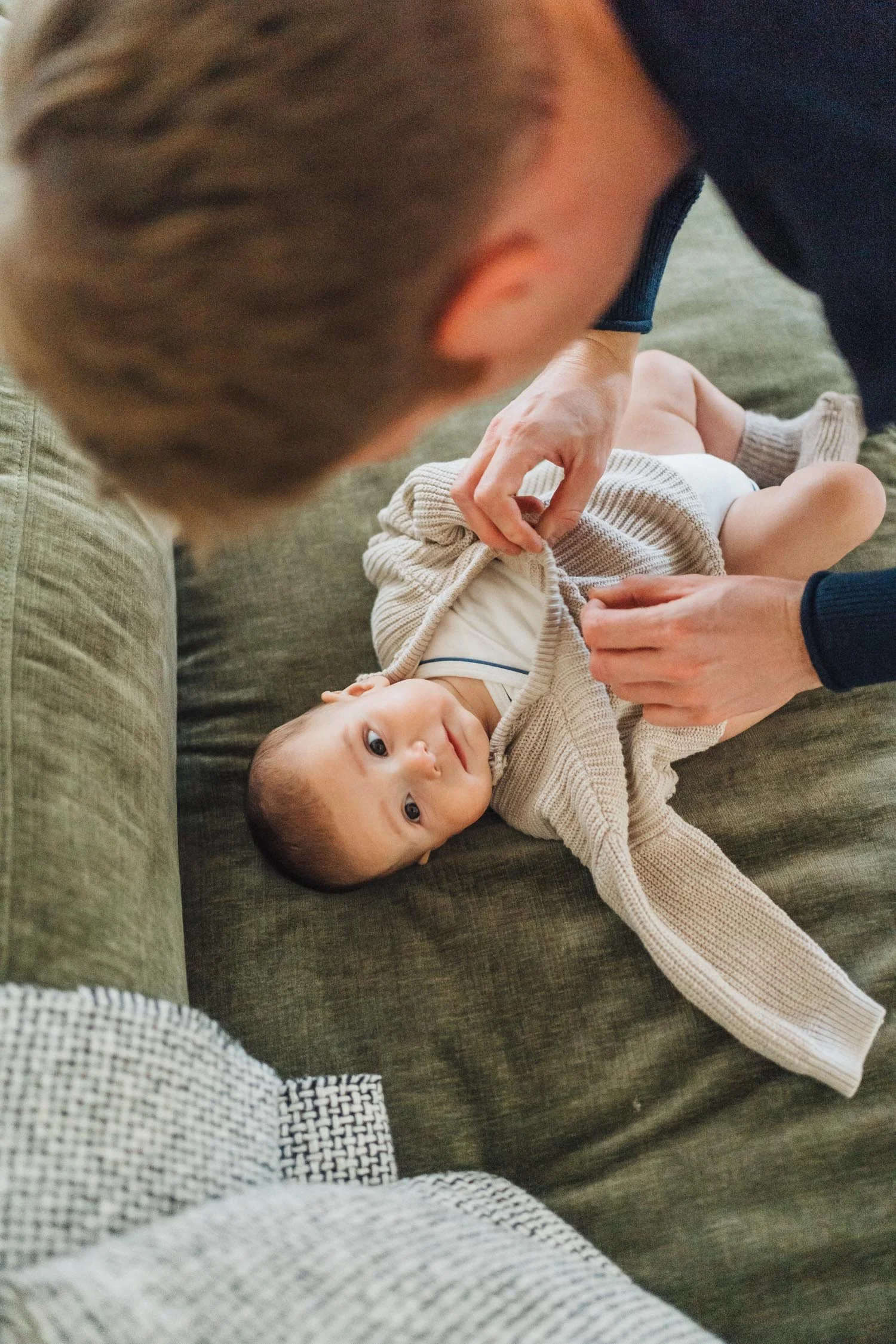 Father changing his baby’s clothes on the sofa during an in-home family photography session in Raleigh–Durham.