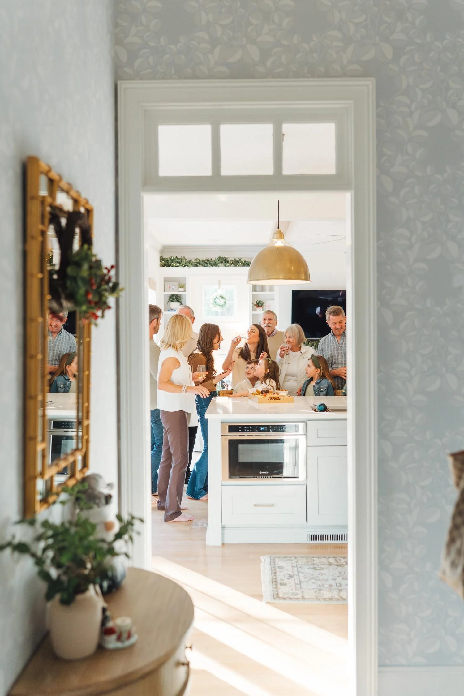 View through a doorway into a kitchen where multiple generations of a family are standing and laughing together during a holiday multi-generational photography session in Raleigh, North Carolina.
