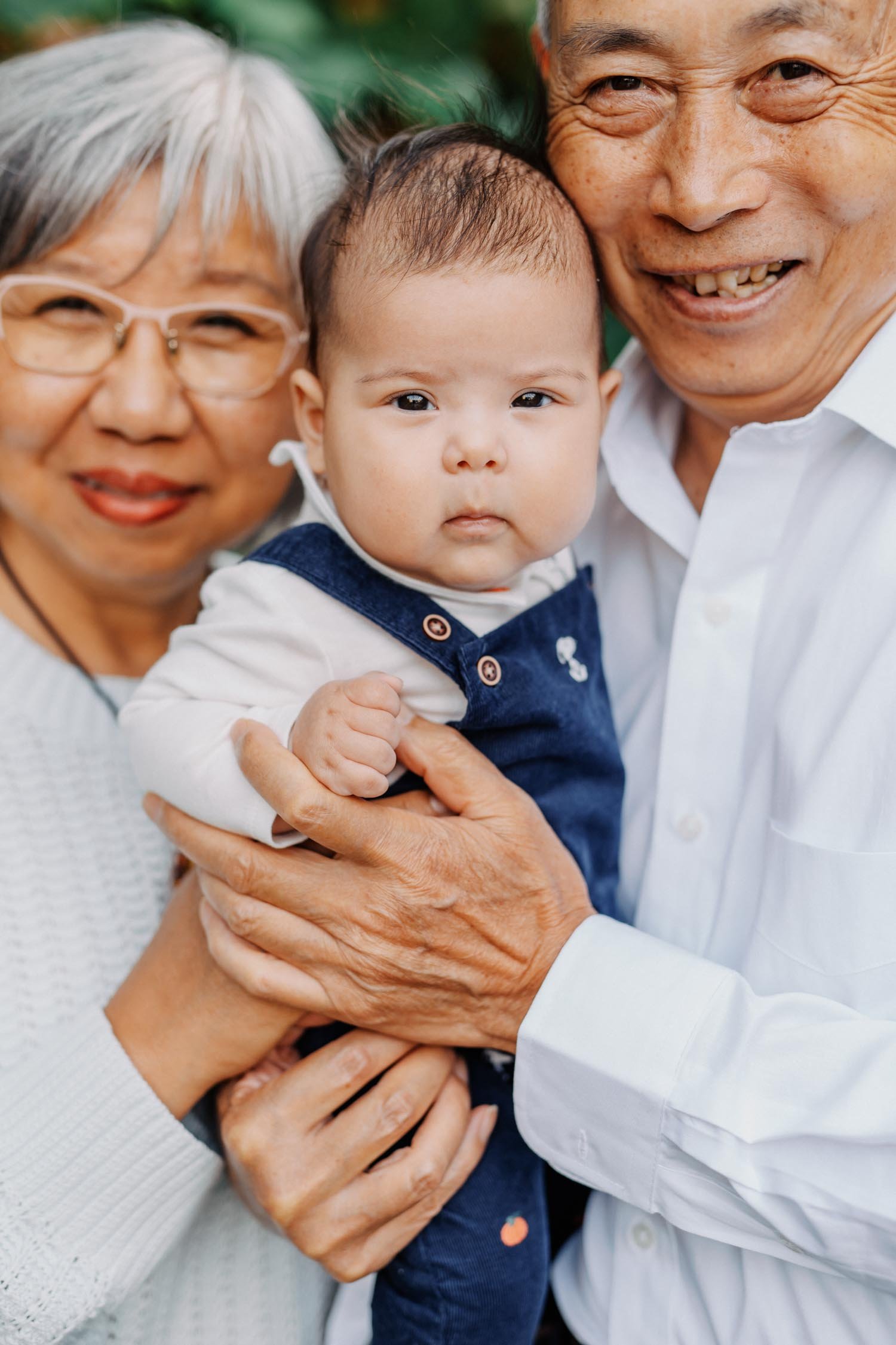 Grandparents smiling while holding their baby grandchild during a multi-generational family photography session in Raleigh, North Carolina.