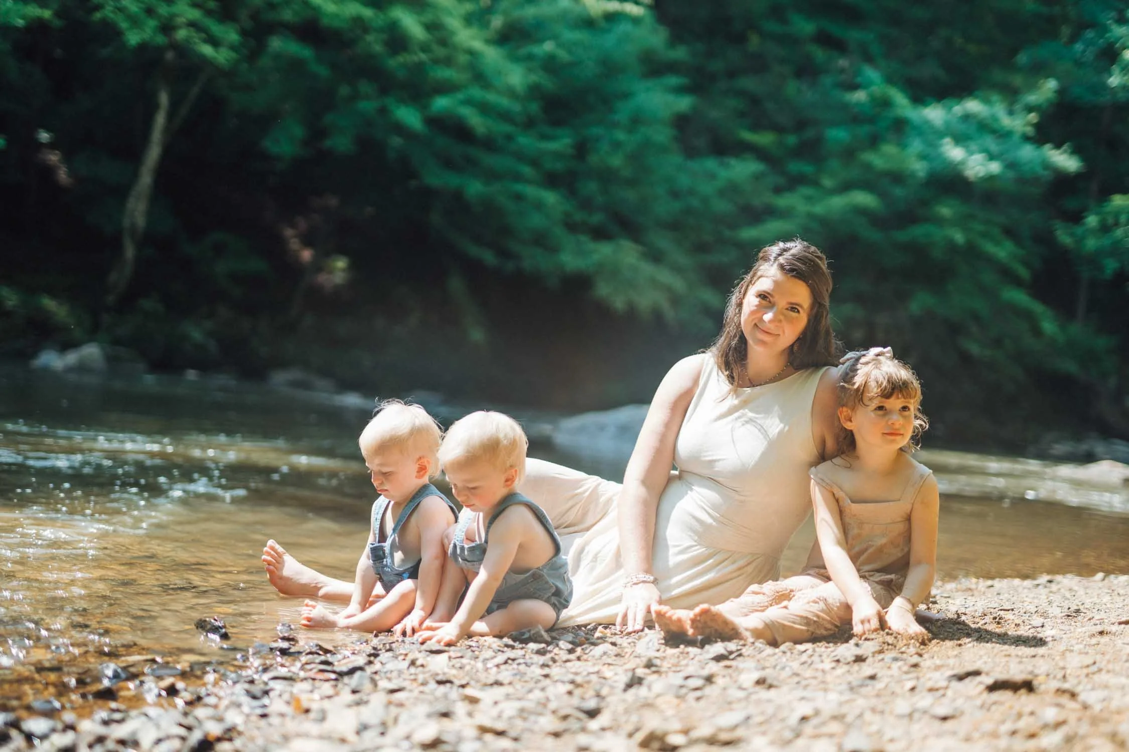 Woman sitting beside a creek with her three young children during a Locals family photography session in Raleigh, North Carolina.