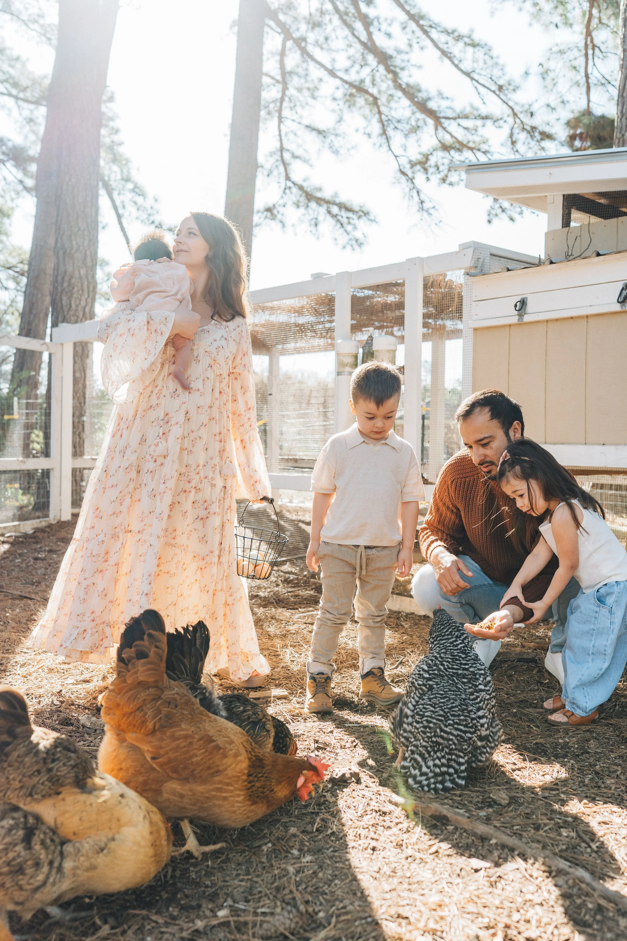 family in chicken coop smiling and playing with newborn and two kids backyard family photos in Raleigh North Carolina