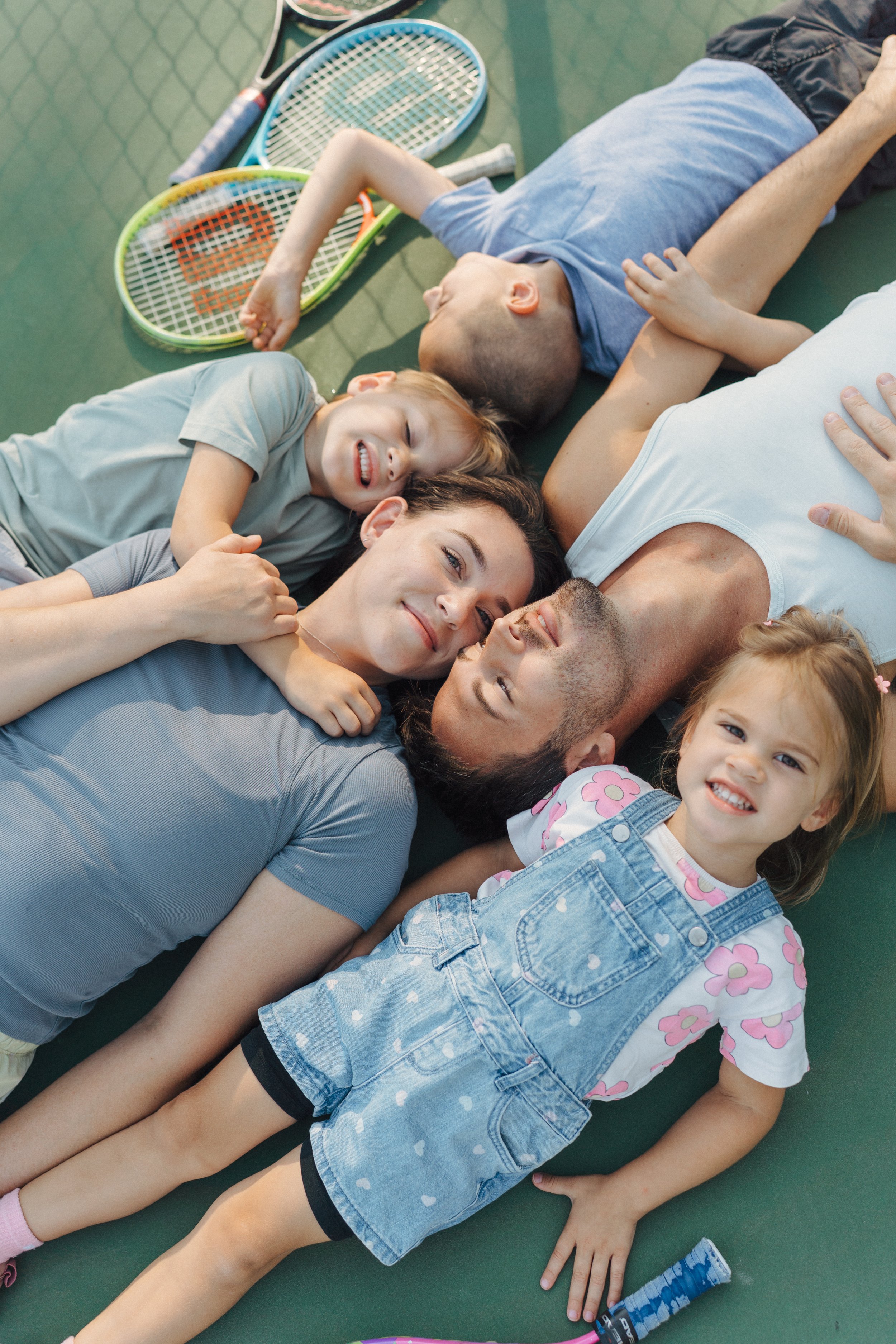 Family of five laying on a tennis court together smiling for storytelling family photos in Raleigh-Durham North Carolina.