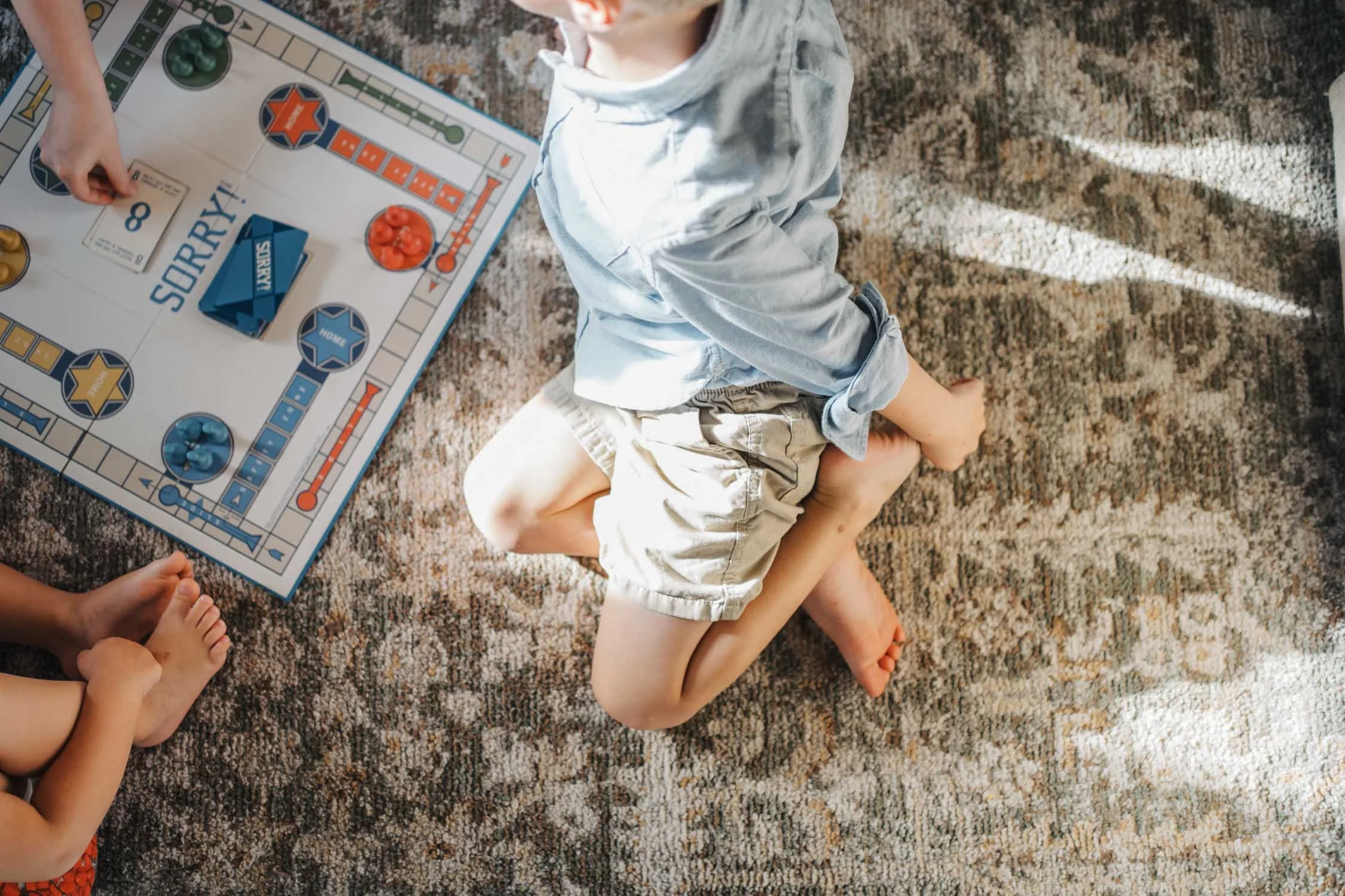 Young children sitting on a rug in the living room playing a board game together during an in-home family photography session.