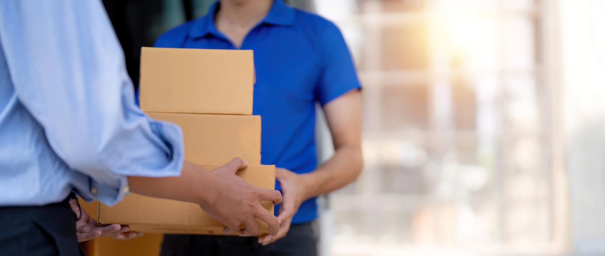 Person in a blue shirt handing over four cardboard boxes to another person in a light blue shirt.