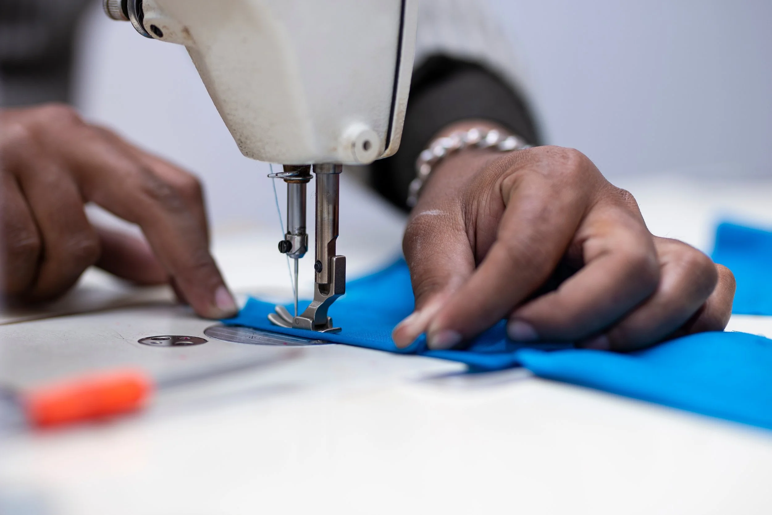 Close-up of hands guiding blue fabric through a sewing machine in a sewing workshop.