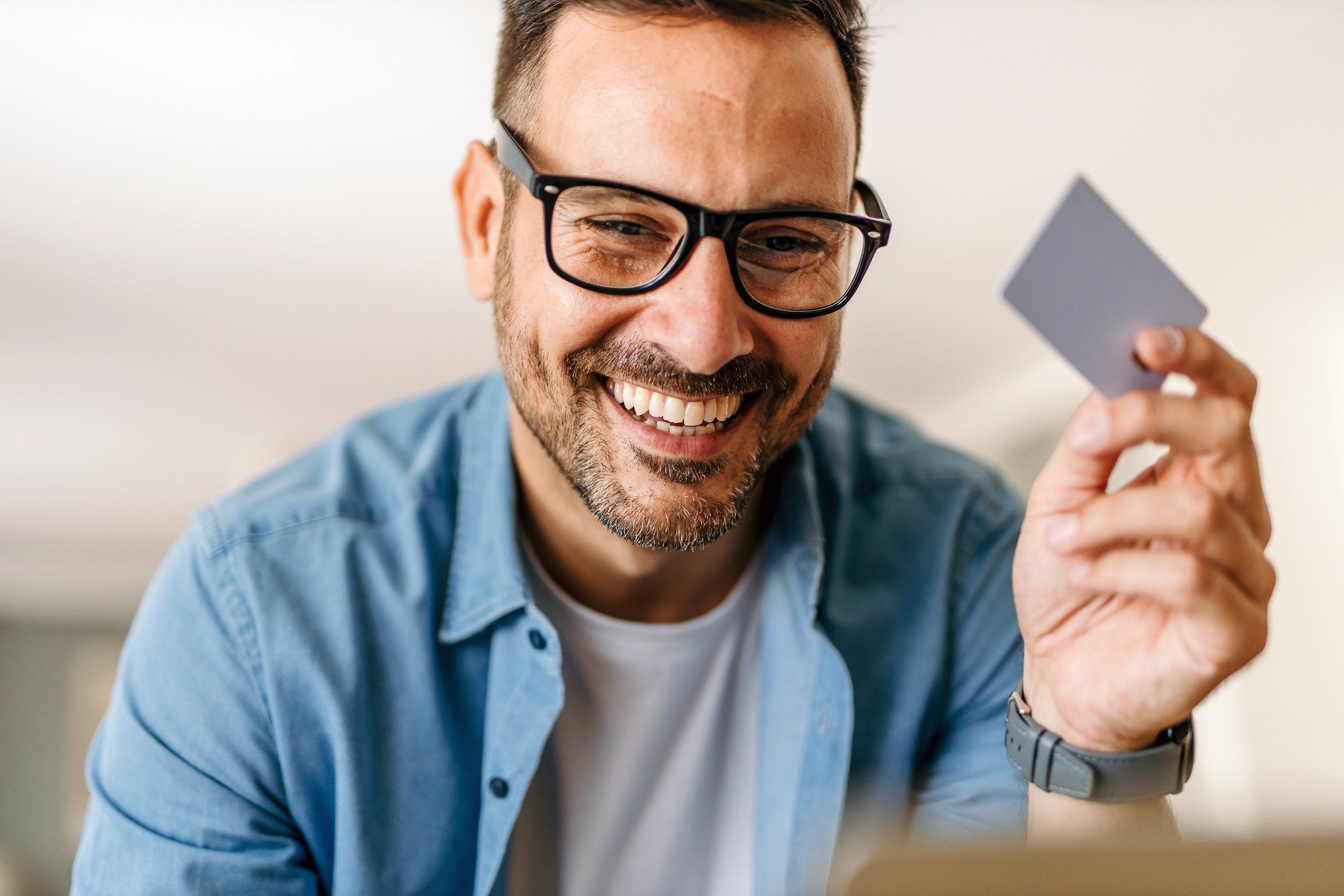 A smiling man with glasses holding a credit card during a video call or online transaction.