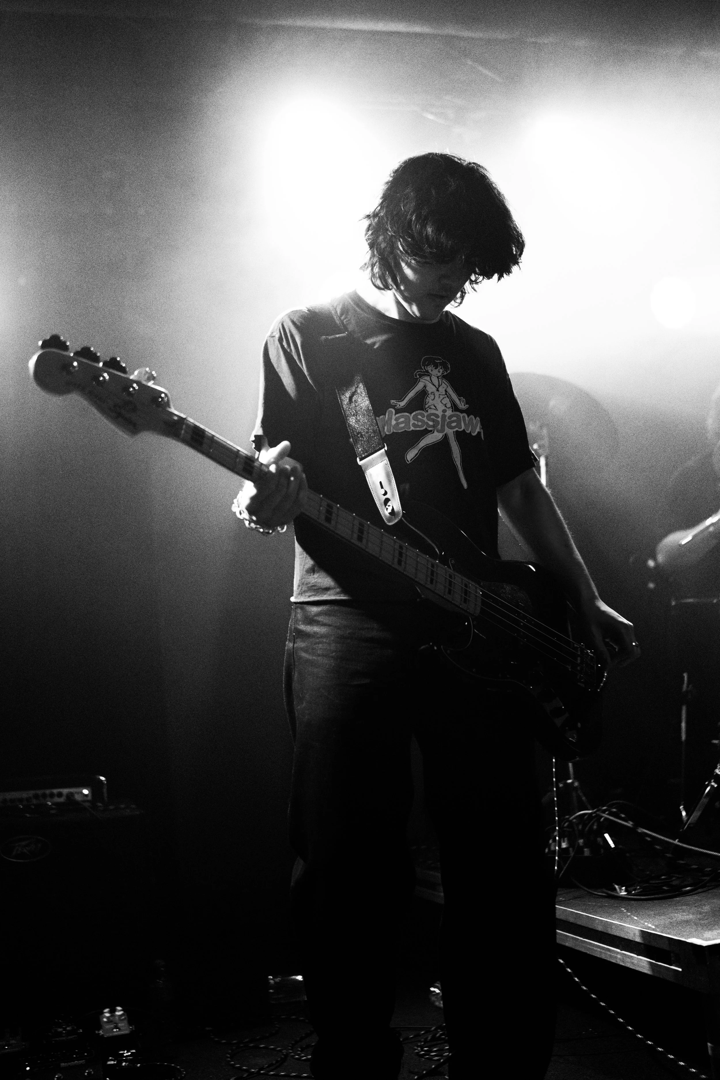 A person playing an electric guitar on stage, illuminated by bright overhead lighting, wearing a dark T-shirt with a graphic.
