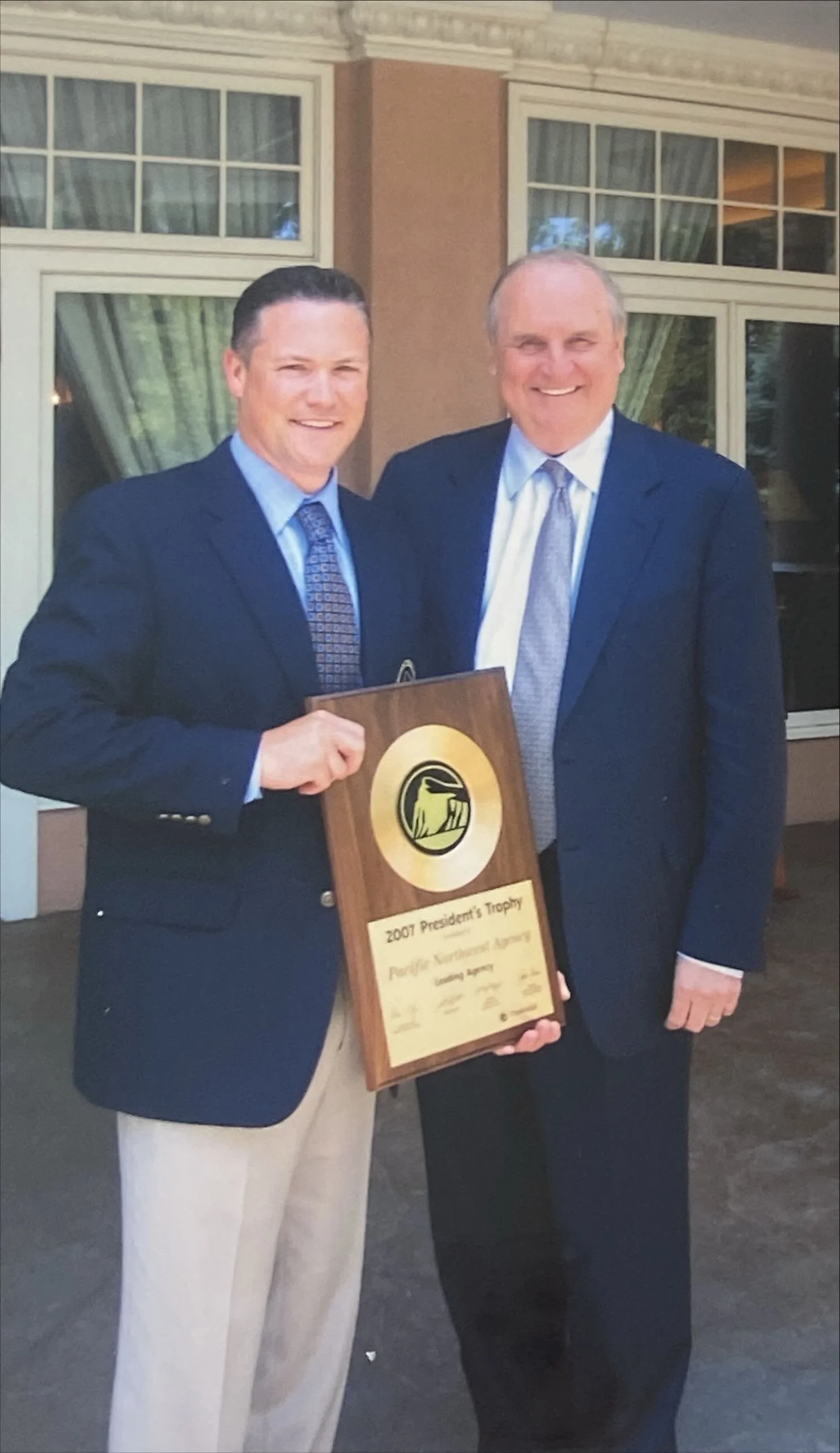 Two men in suits standing outside holding a plaque that reads "2007 President's Trophy."