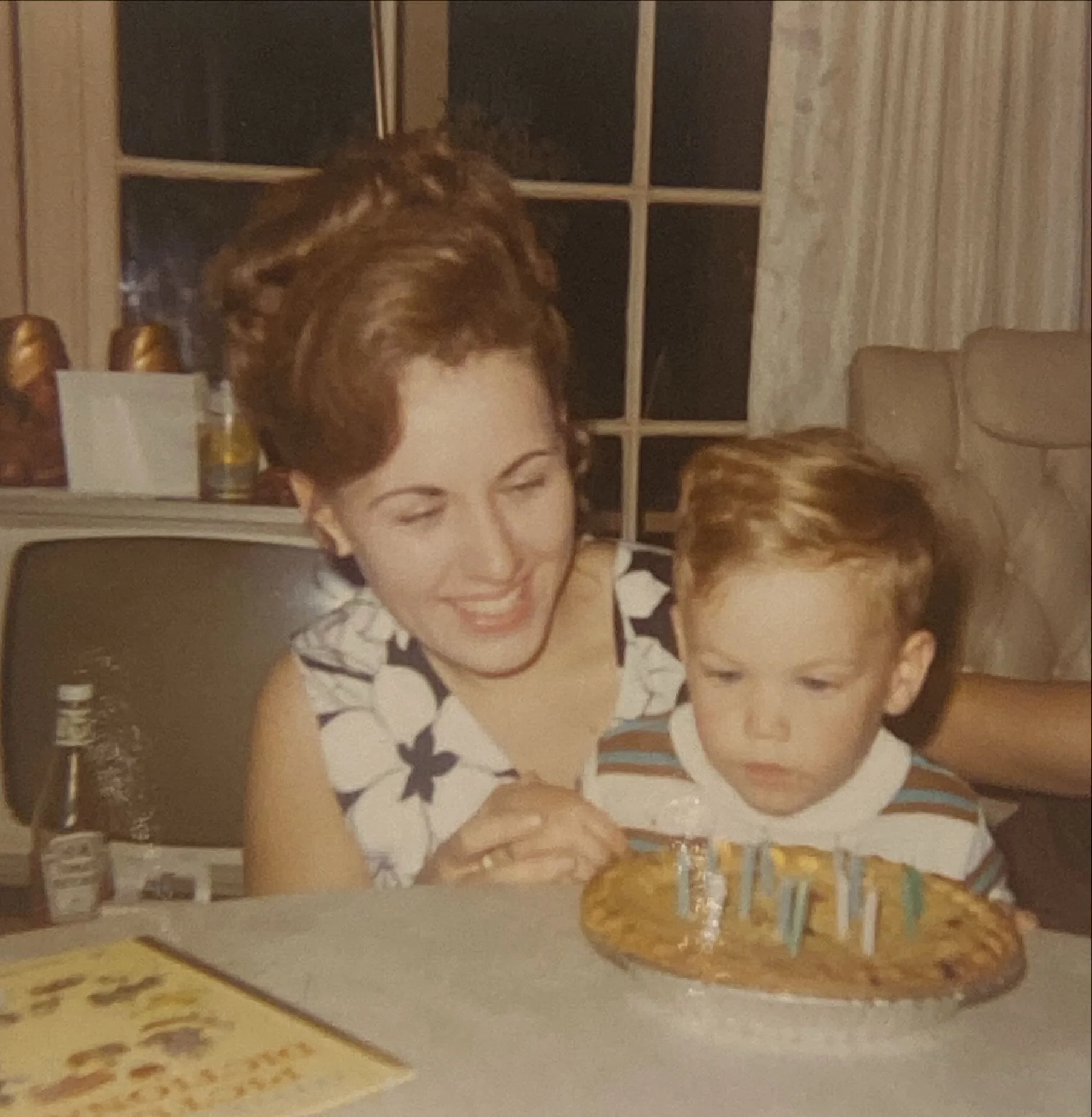 A woman and a young boy with red hair celebrating a birthday with a cake and candles.