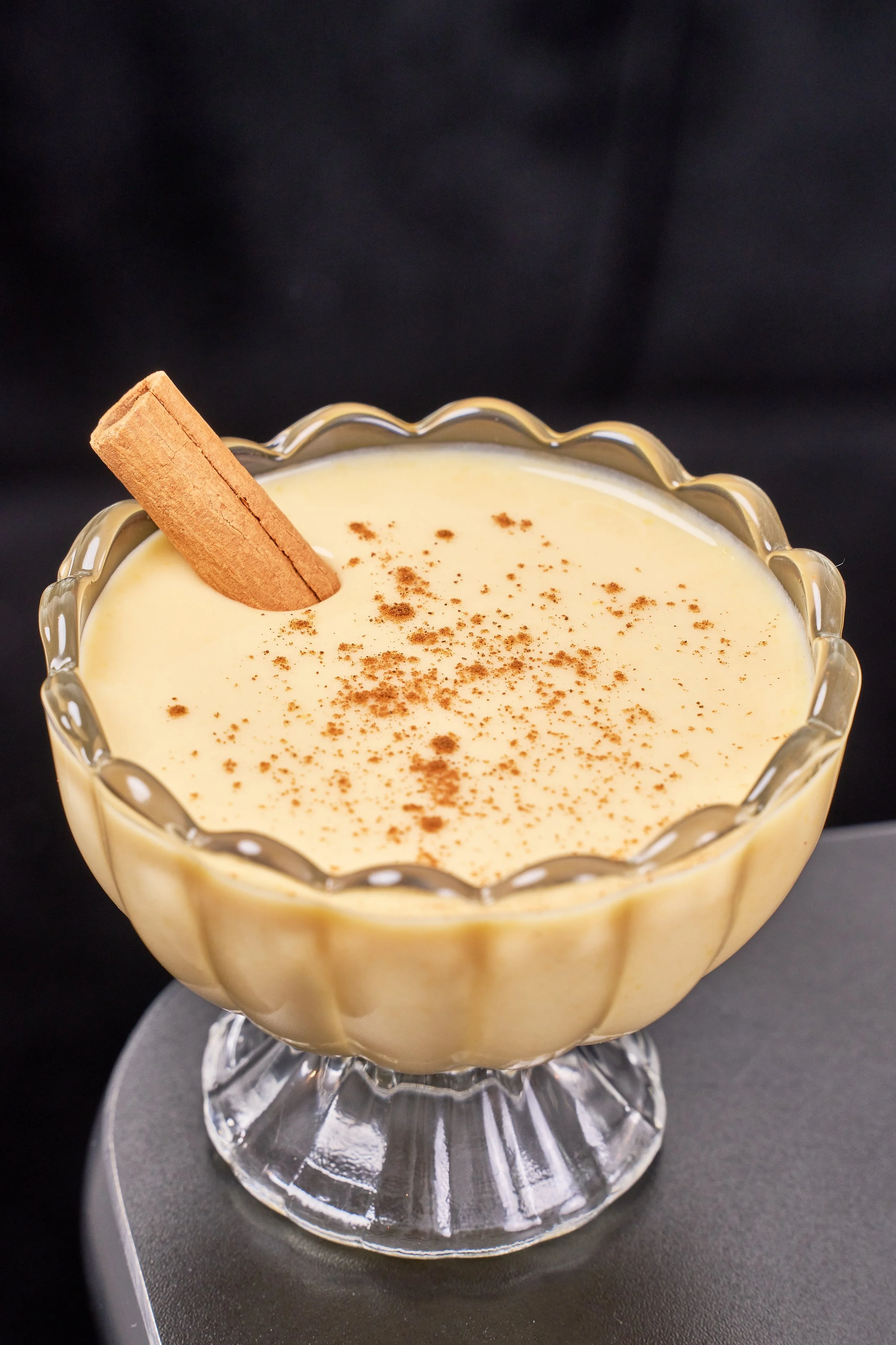 Creamy pudding topped with cinnamon powder and a cinnamon stick in a glass dessert bowl.