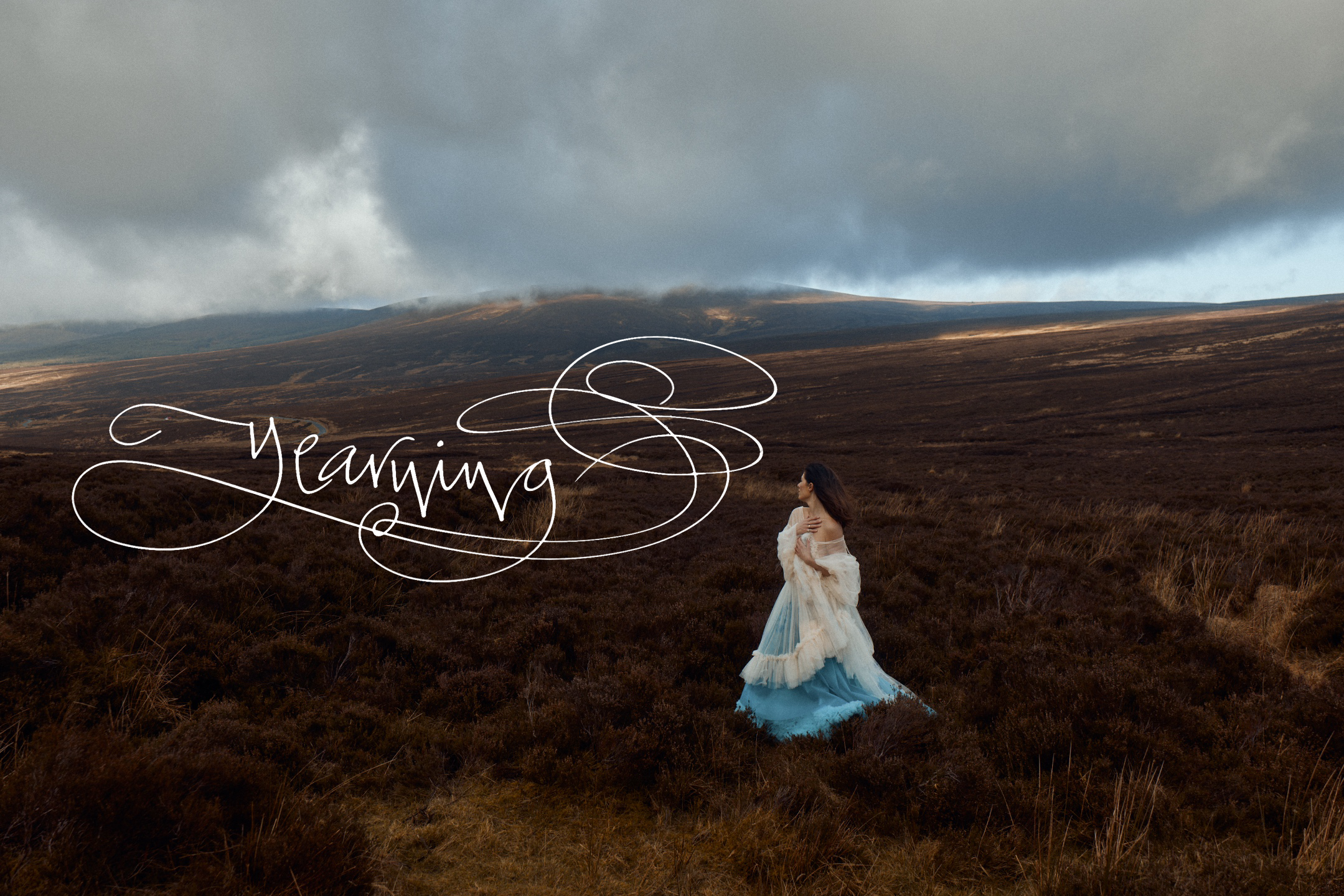 A woman in a blue and white dress walking through a vast, open landscape with rolling brown hills and dark cloudy sky, with the word 'Yearning' written in elegant cursive overlay.