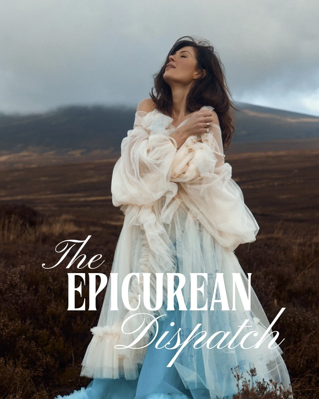 A woman in a flowing, sheer white dress standing outdoors in a field with a mountain and cloudy sky in the background. The text overlays say "The EpiCurean Dispatch."