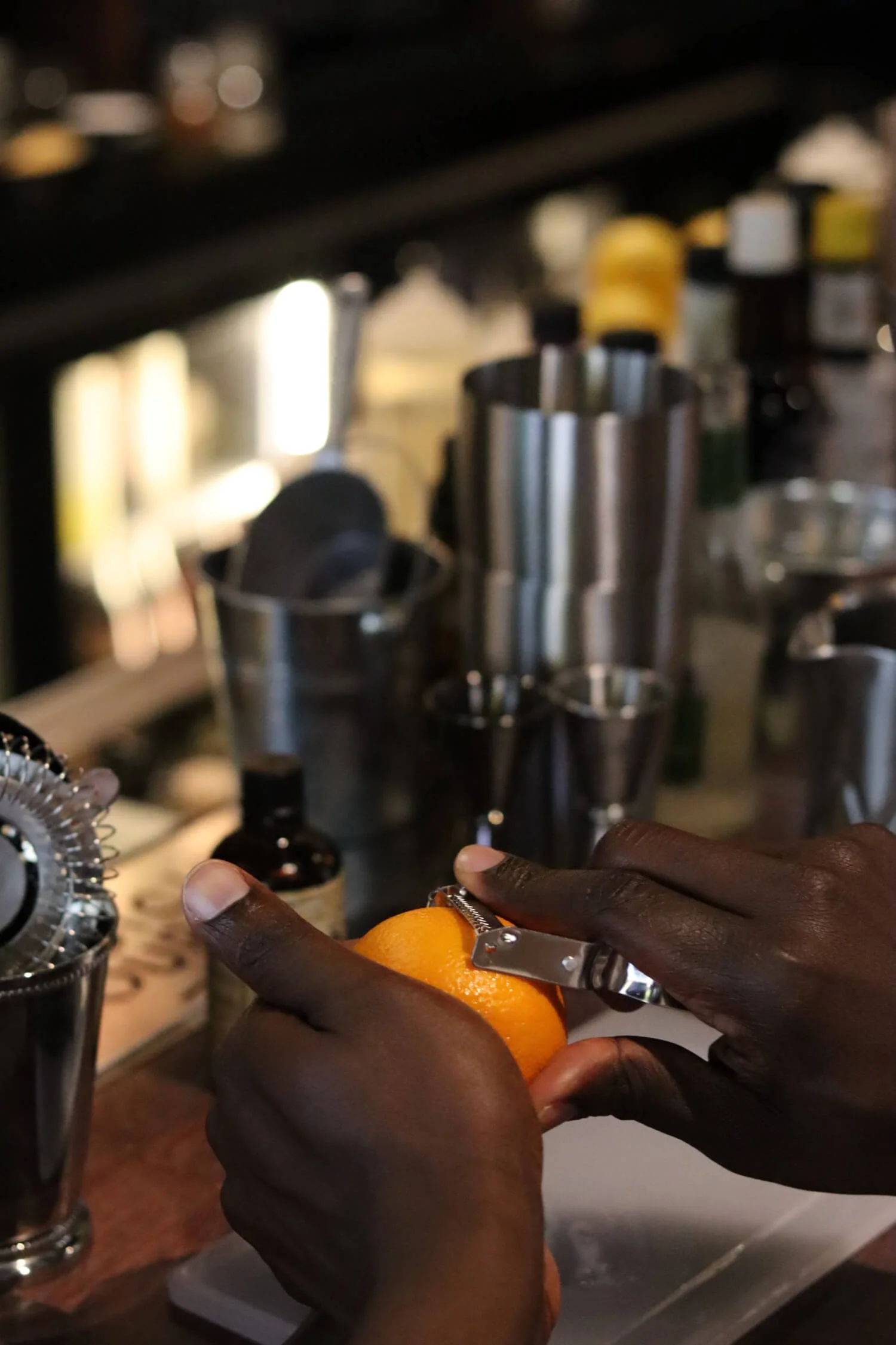 Person zesting an orange at a bar with various bottles and bar tools in the background.