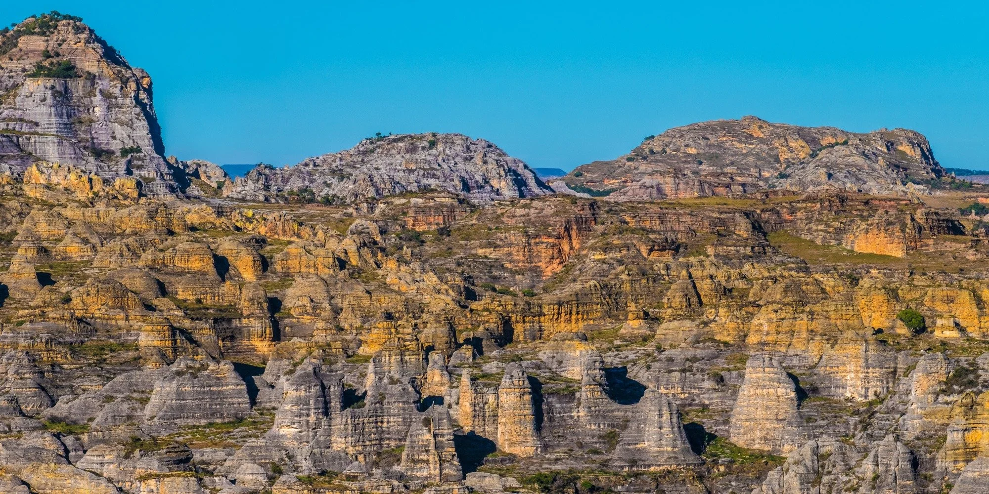 A rugged mountain landscape with layered rock formations under a clear blue sky.